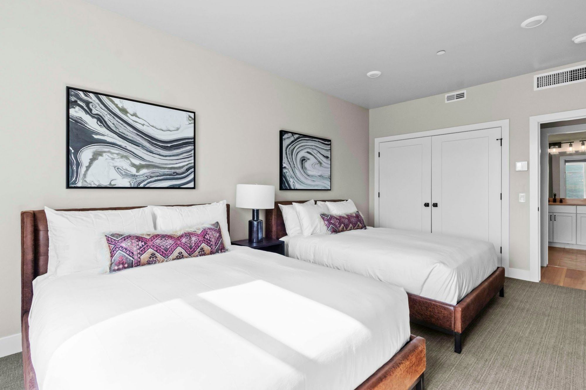 image Two queen beds with brown leather headboards, white bedding, and abstract wall art