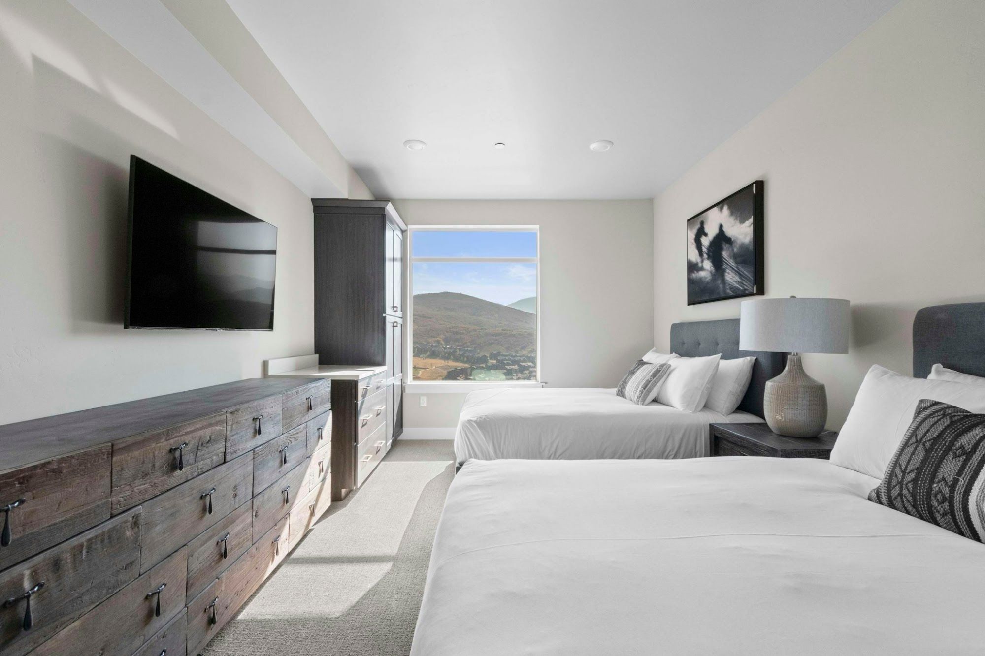 image Two queen beds with white bedding, wall-mounted TV, and framed mountain view
