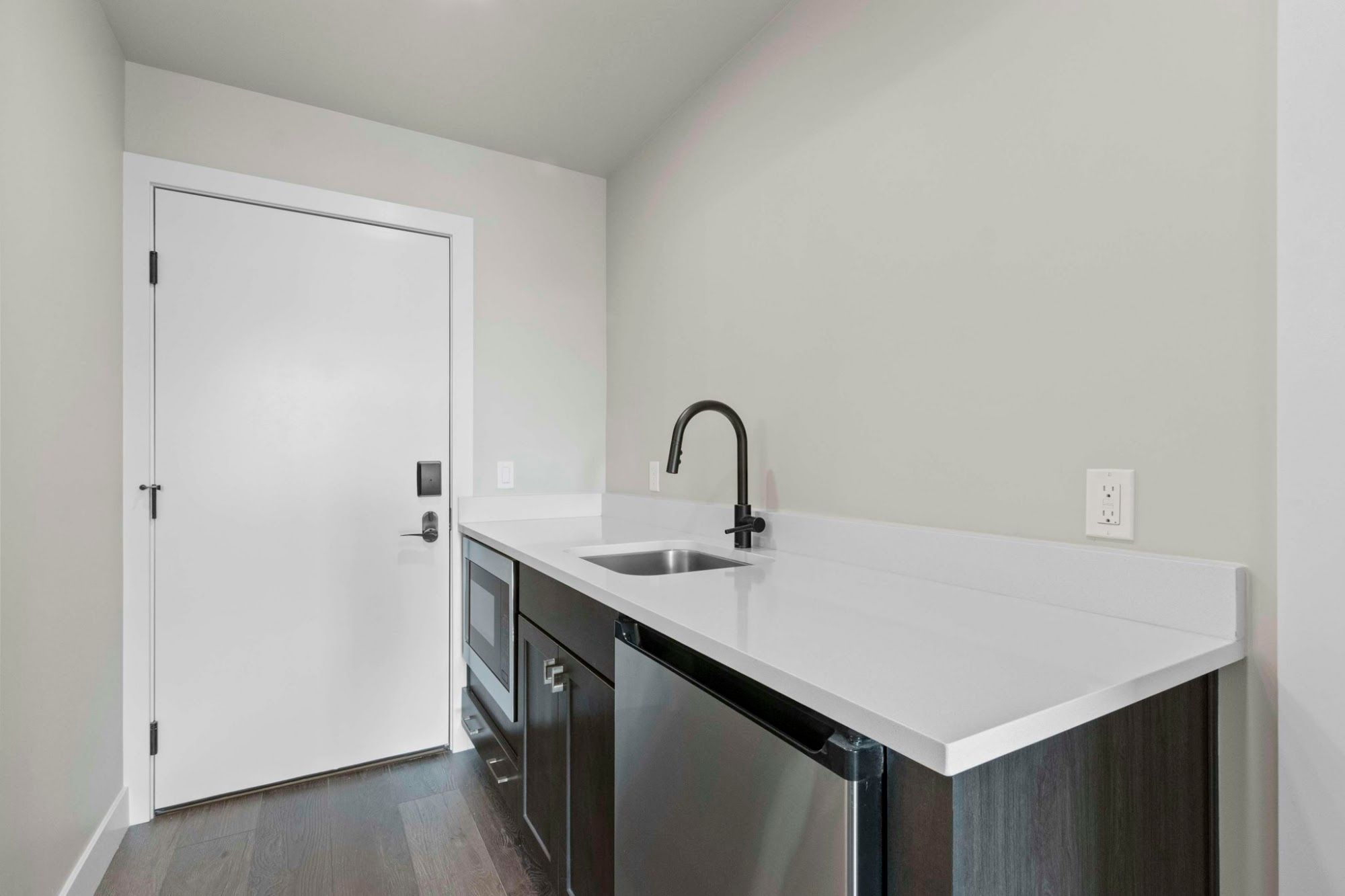 image Wet bar with white quartz countertop, undermount sink, built-in microwave, and mini-fridge