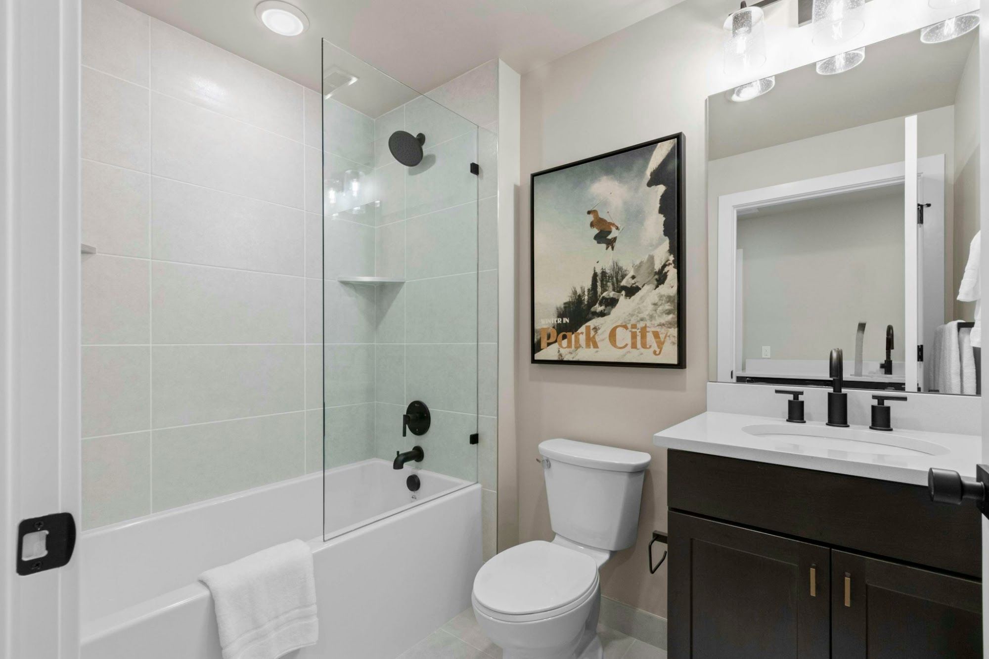 image Full bathroom with tub-shower combination, glass door, dark wood vanity, and ski art