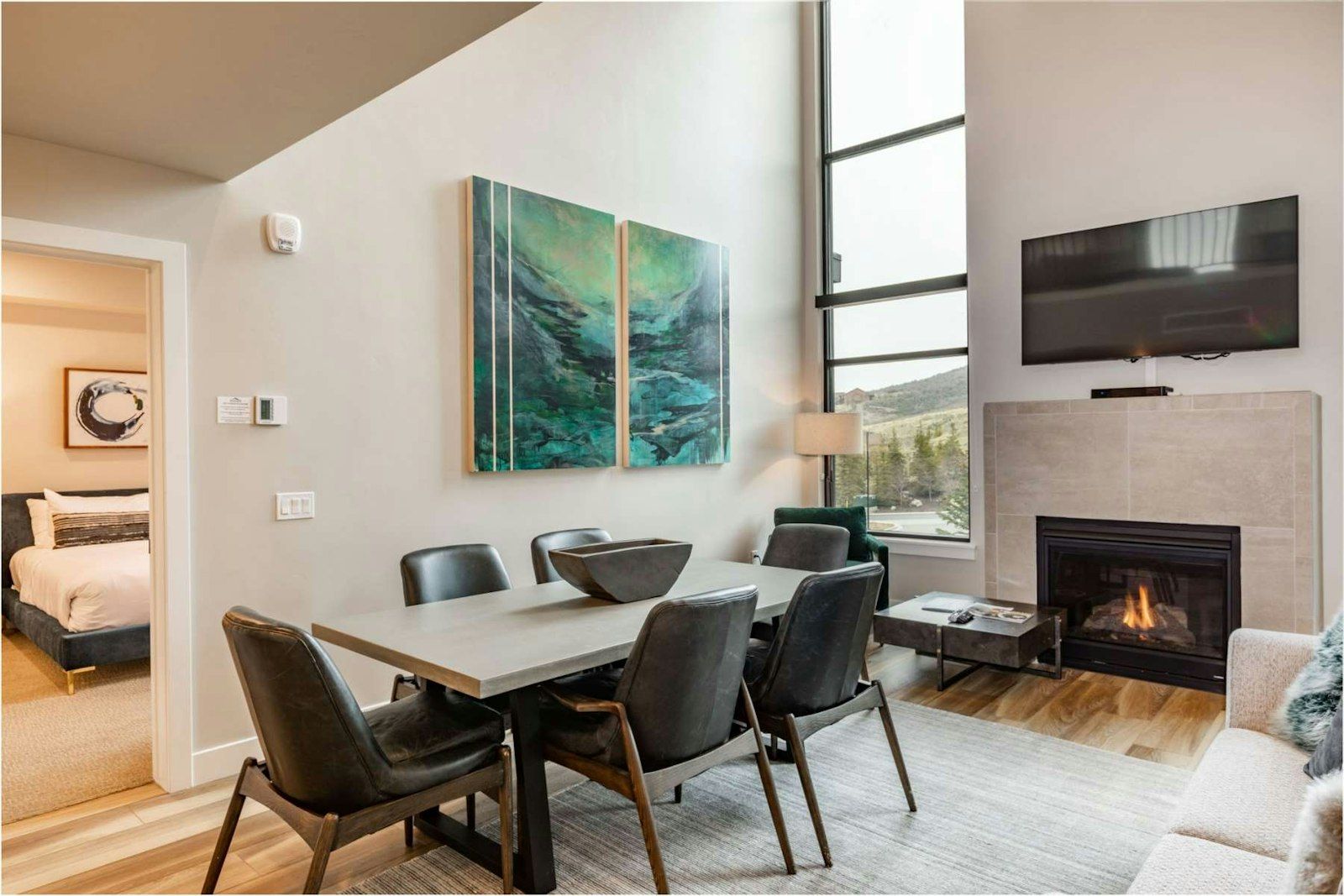 image Open-plan great room with dining table, fireplace, and floor-to-ceiling mountain-view windows