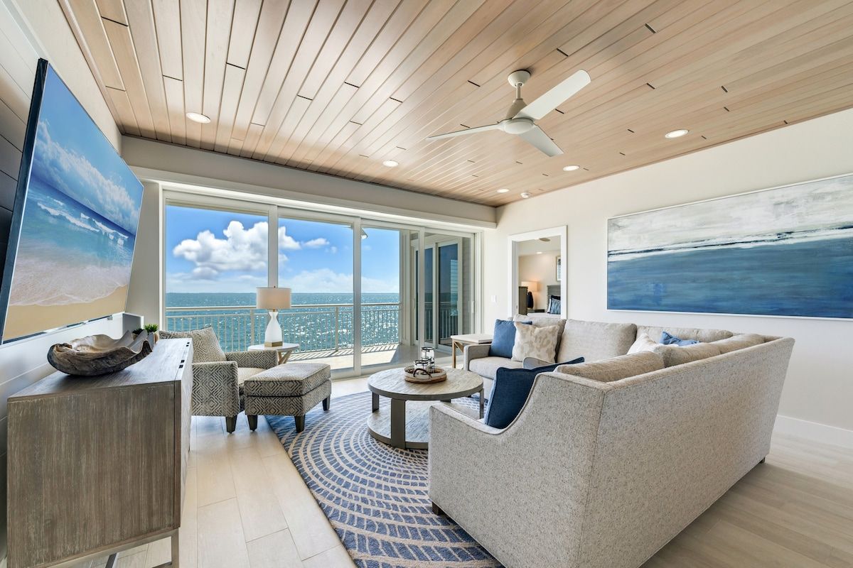 image Bright oceanfront living room with comfortable seating, a TV, and direct access to a furnished balcony.
