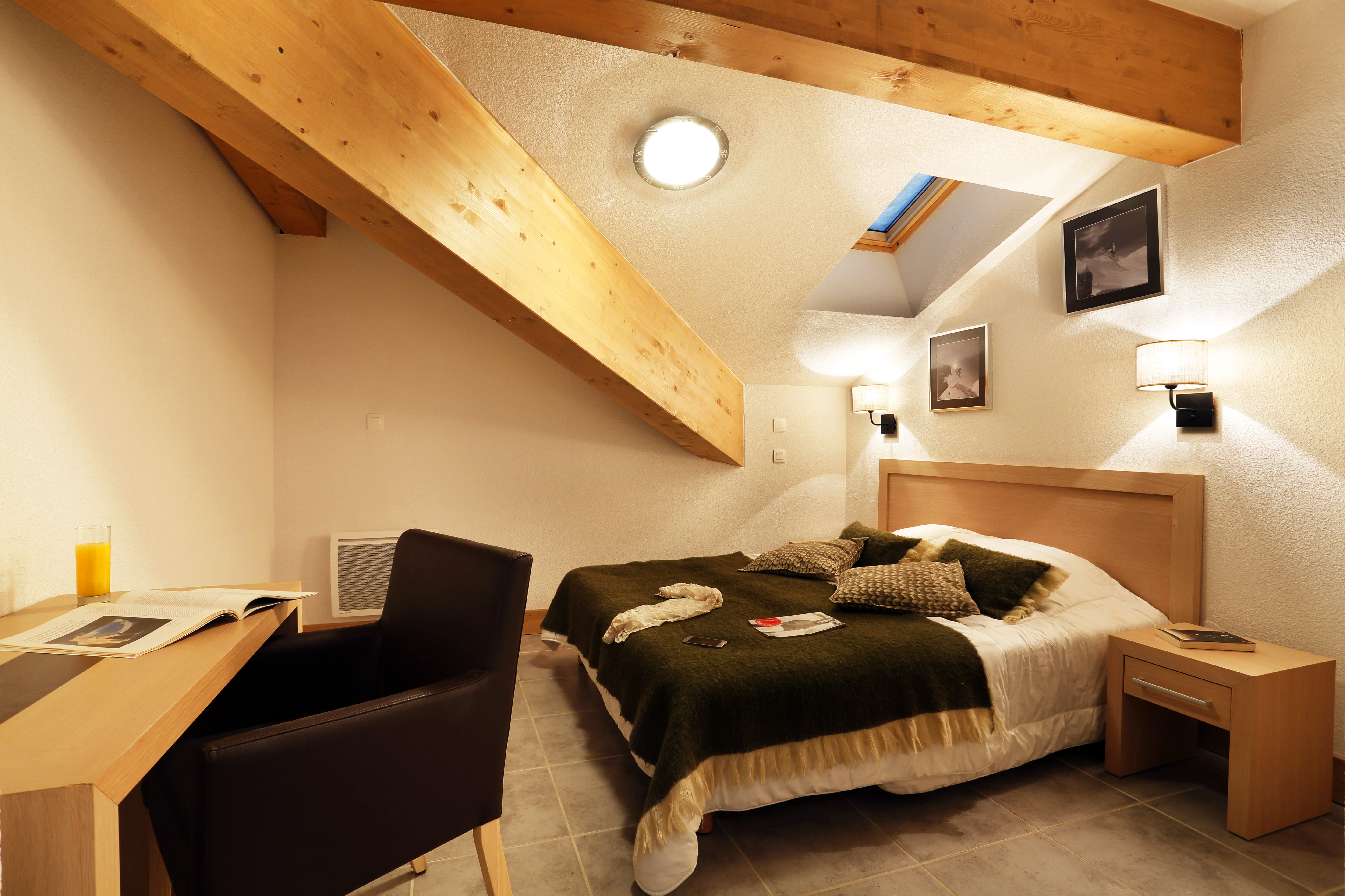 image The double bed sits beneath exposed wood beams and a skylight, with black-and-white ski photography on the walls.