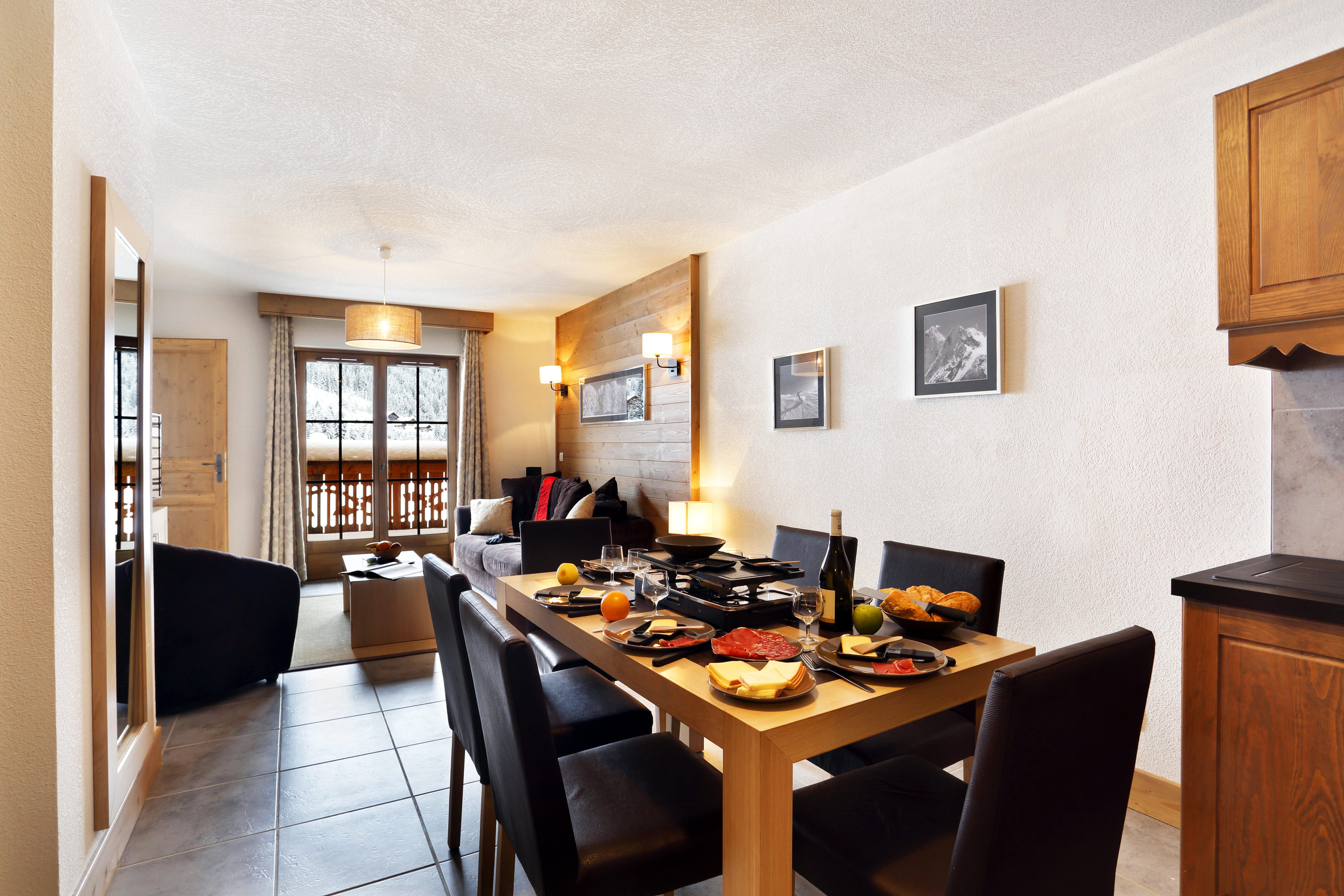 image A raclette set and Savoyard charcuterie cover the dining table, seating six beneath black-and-white mountain prints.