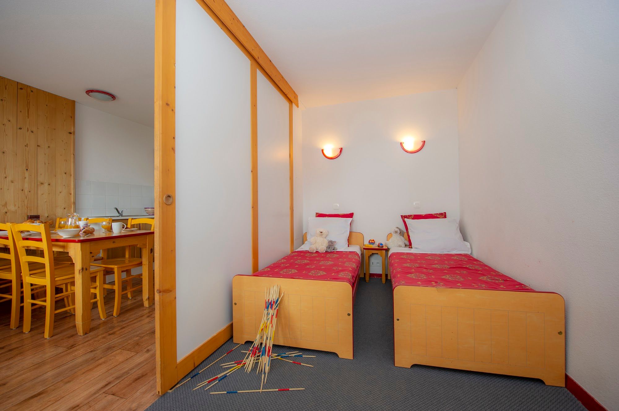image Bedroom with two single beds and toys, kitchen visible nearby.