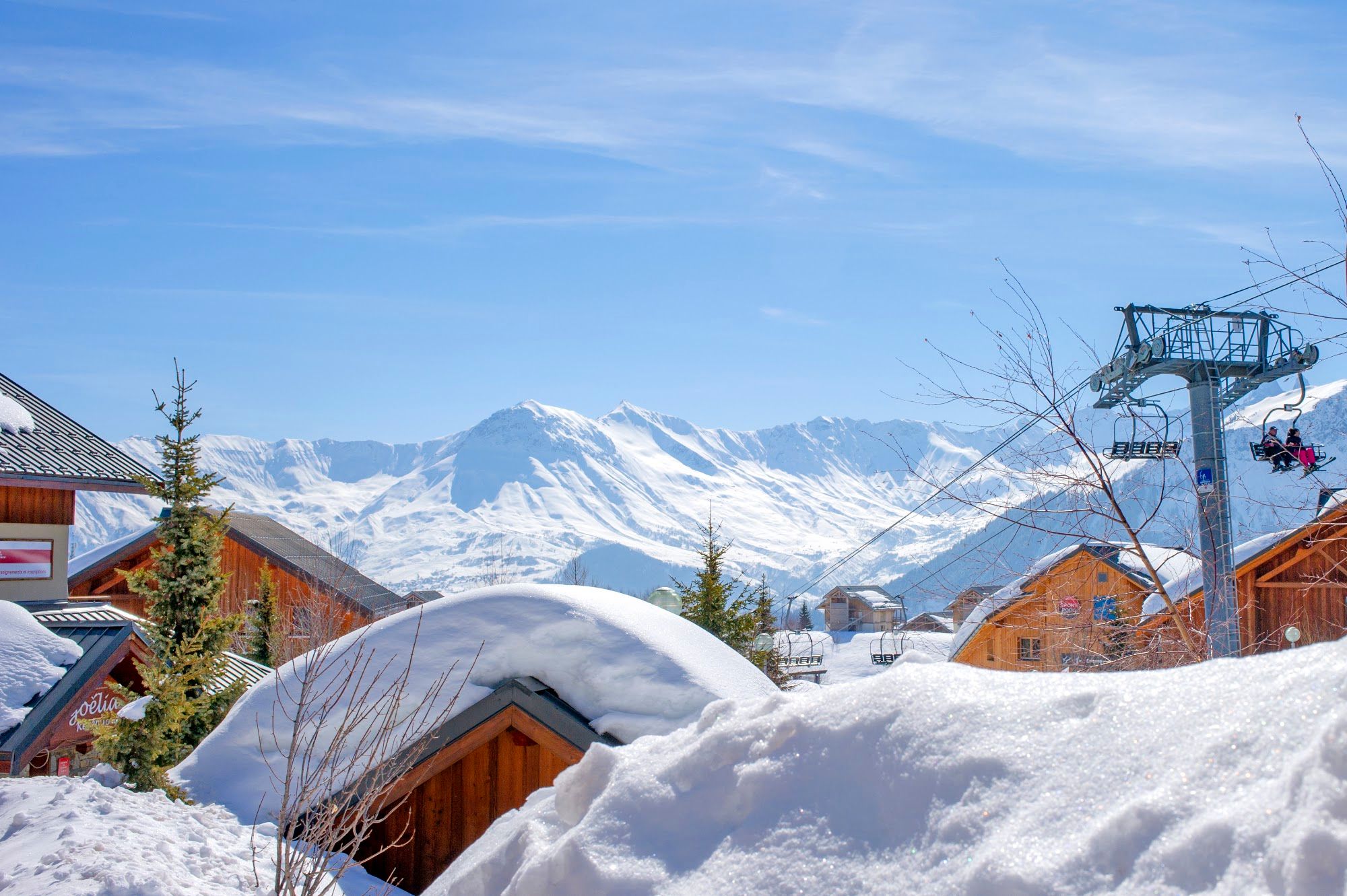 image A snowy landscape with wooden buildings and a ski lift against a mountain backdrop.