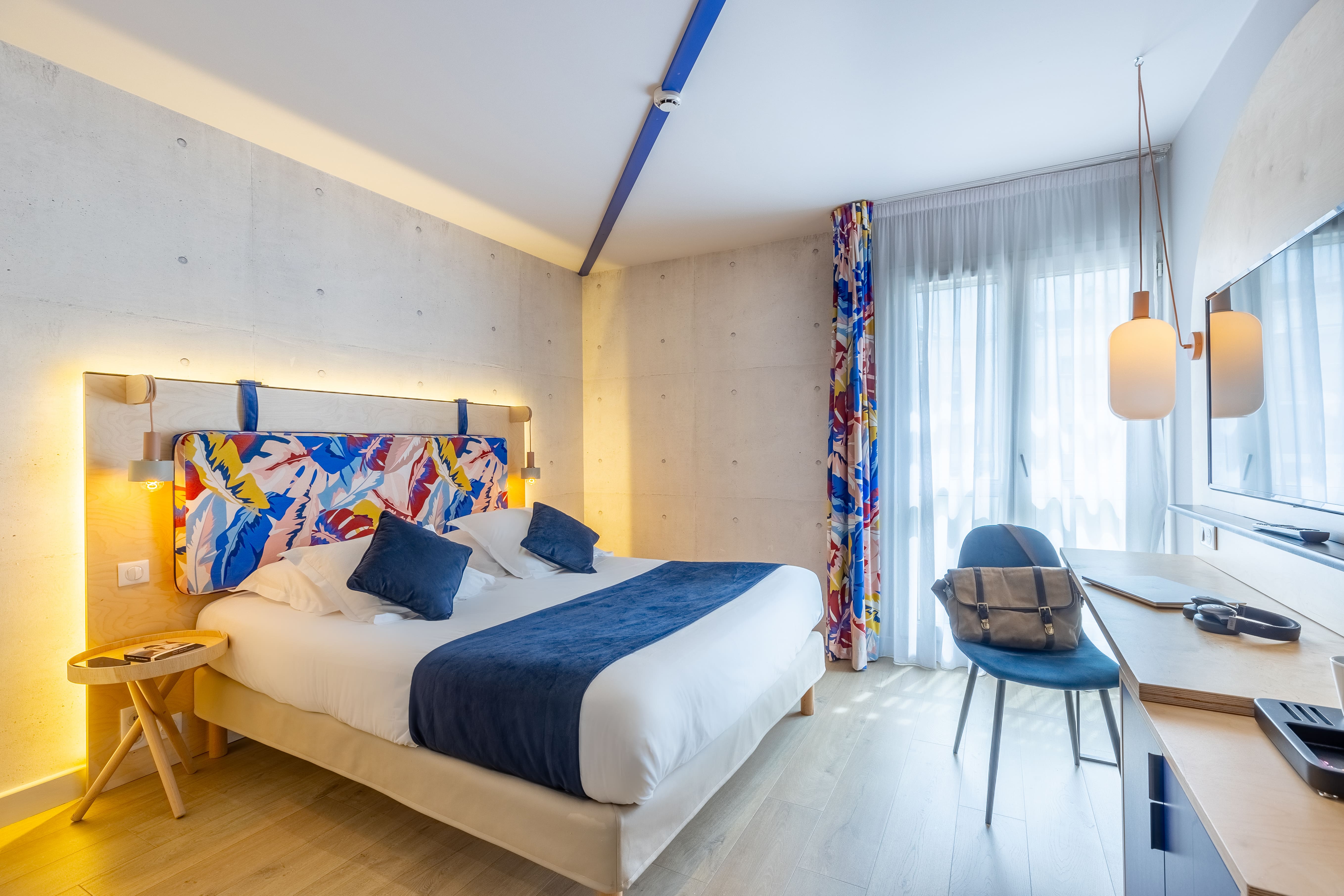 image Exposed concrete walls frame the bed's colourful headboard, with a desk and flat-screen TV for evenings in