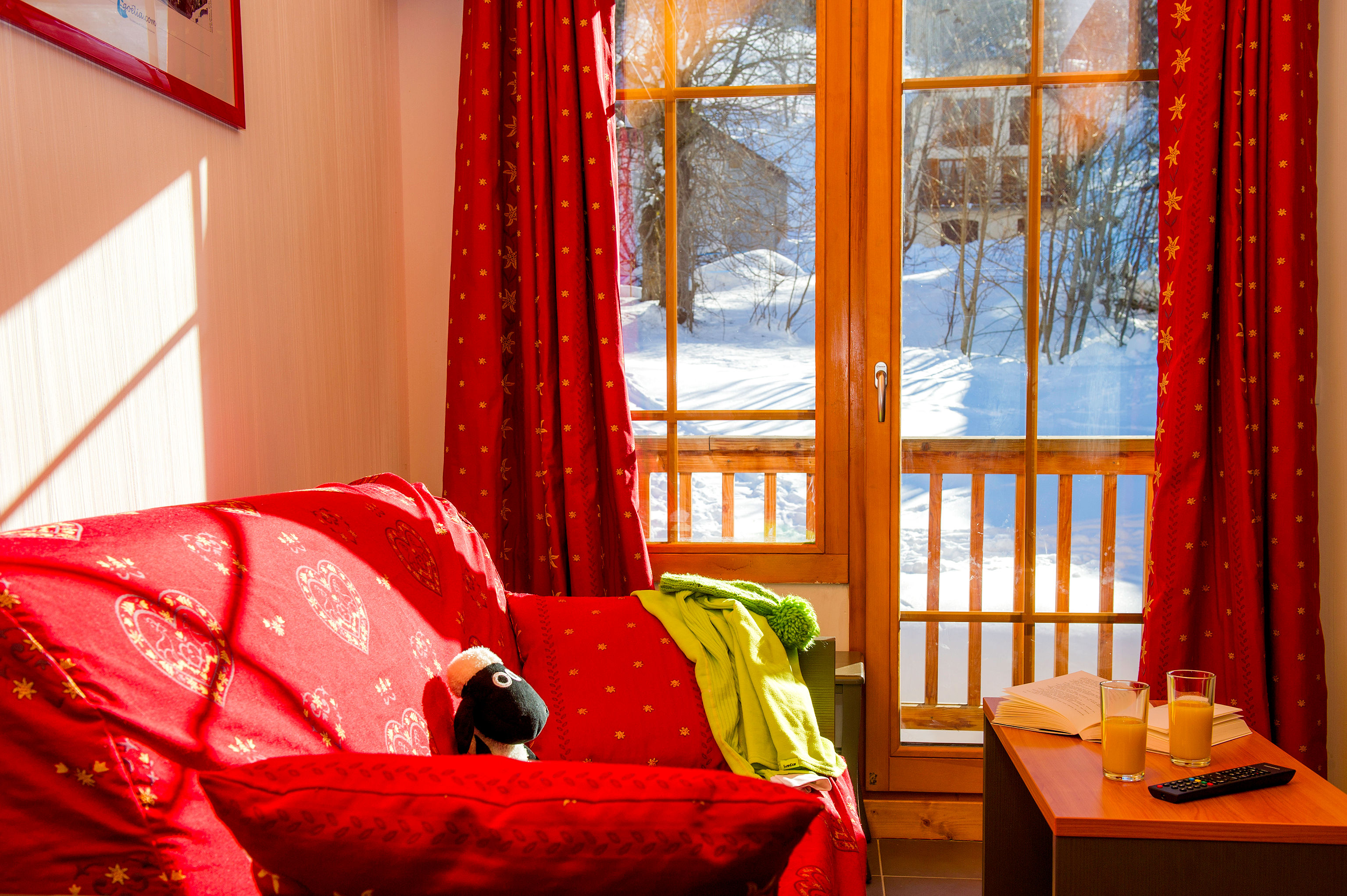 image A red sofa sits beneath bright curtains and large windows.