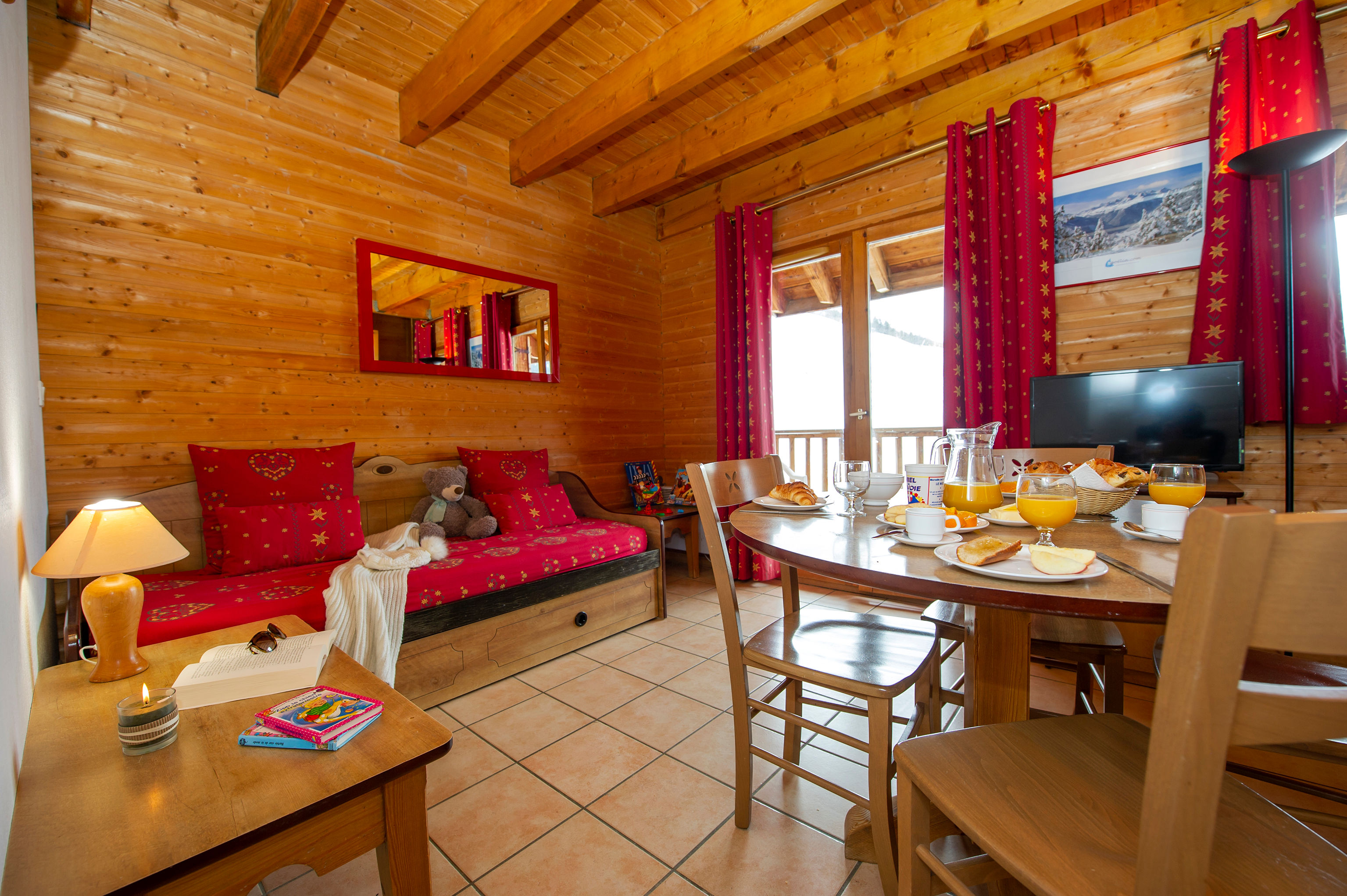 image Sunlight filters past red curtains onto the dining table, with the piste visible through the balcony window.