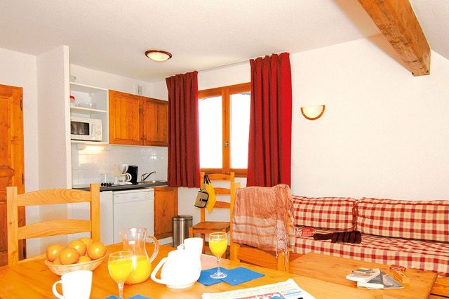 image Kitchenette with wooden cabinetry opens onto the dining table and checkered sofa.