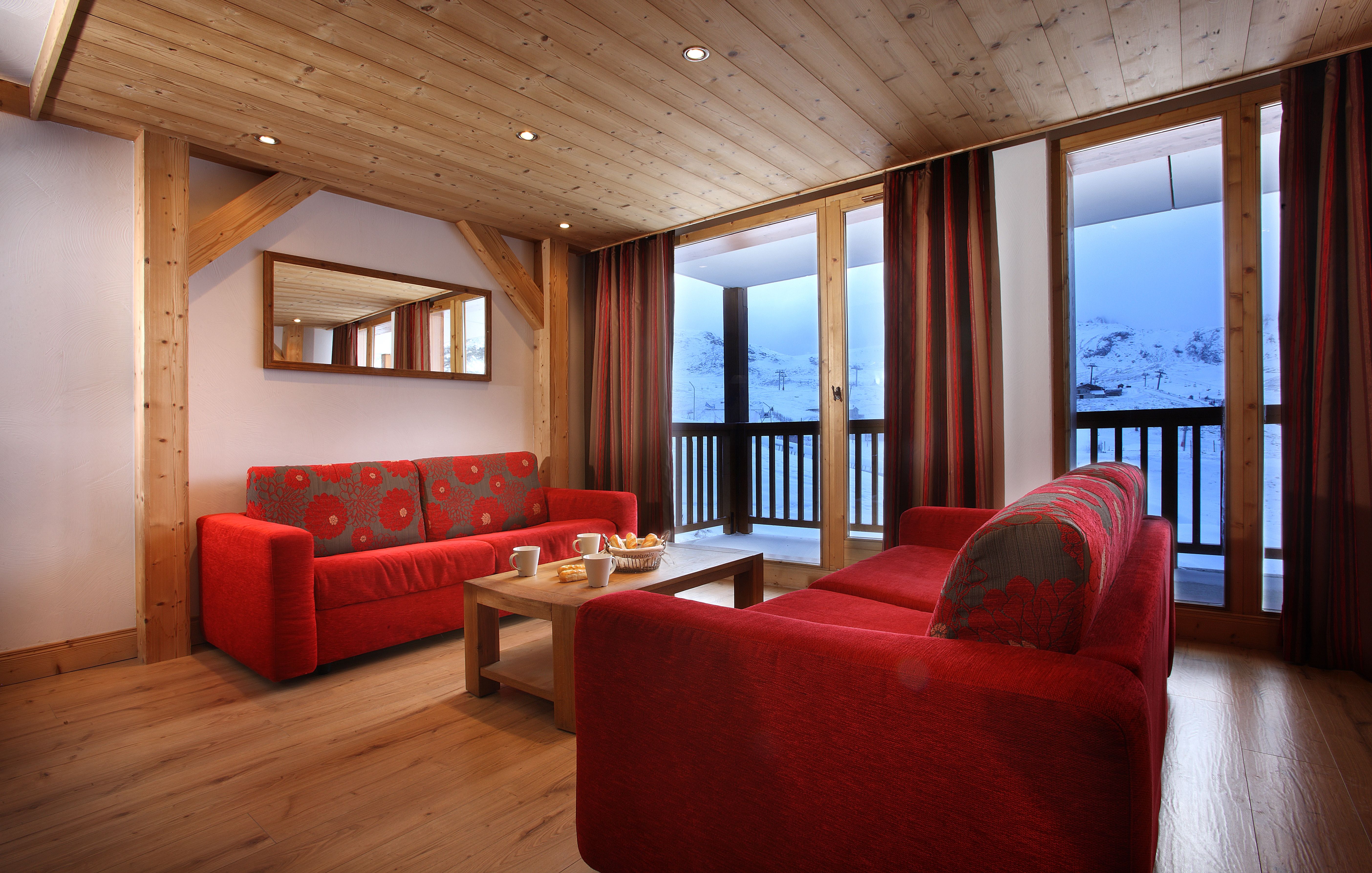image Living room with red sofas and balcony doors opening onto a snowy mountain view.