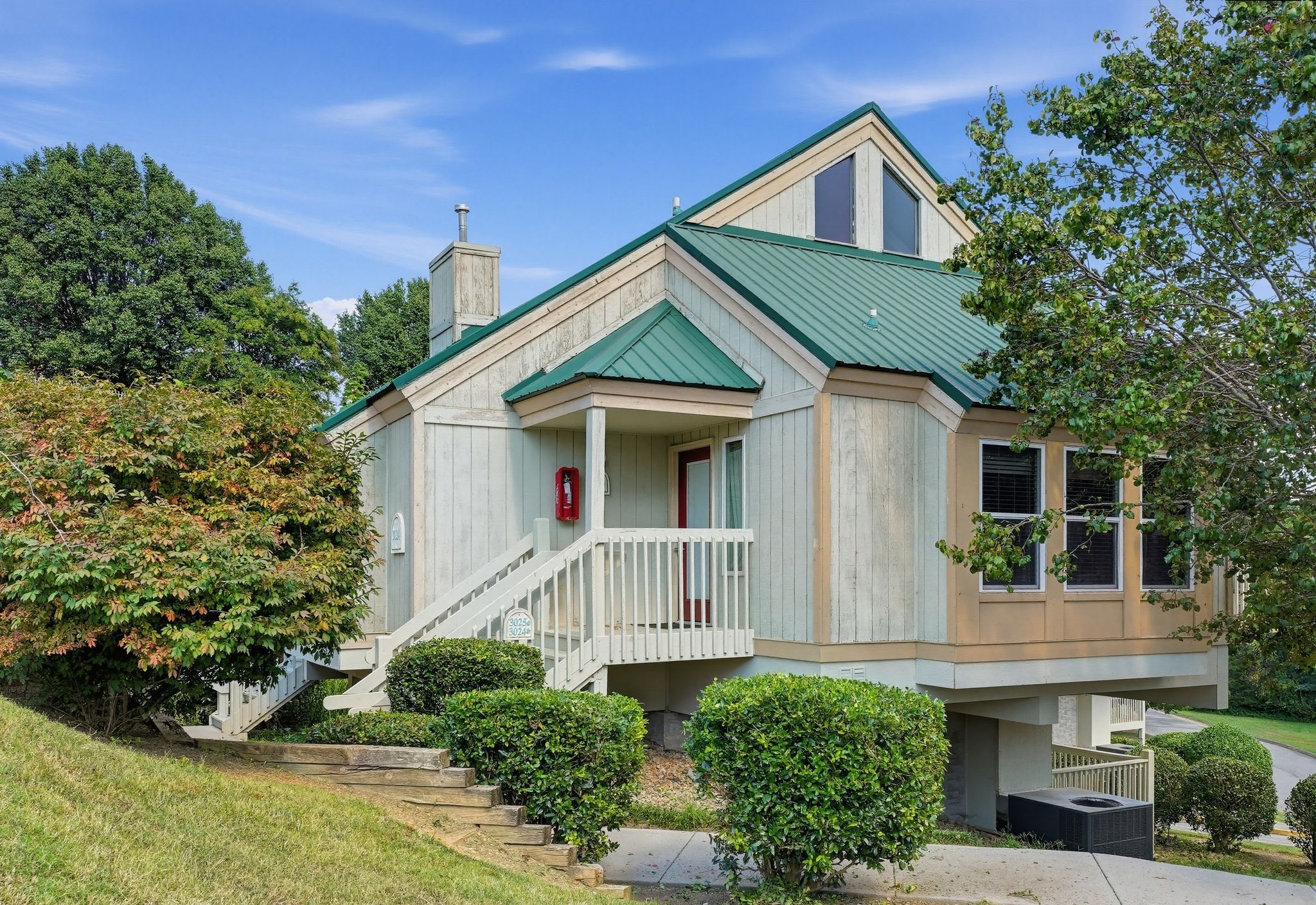 image Two-story townhouse exterior with a green metal roof and a covered entry with stairs.