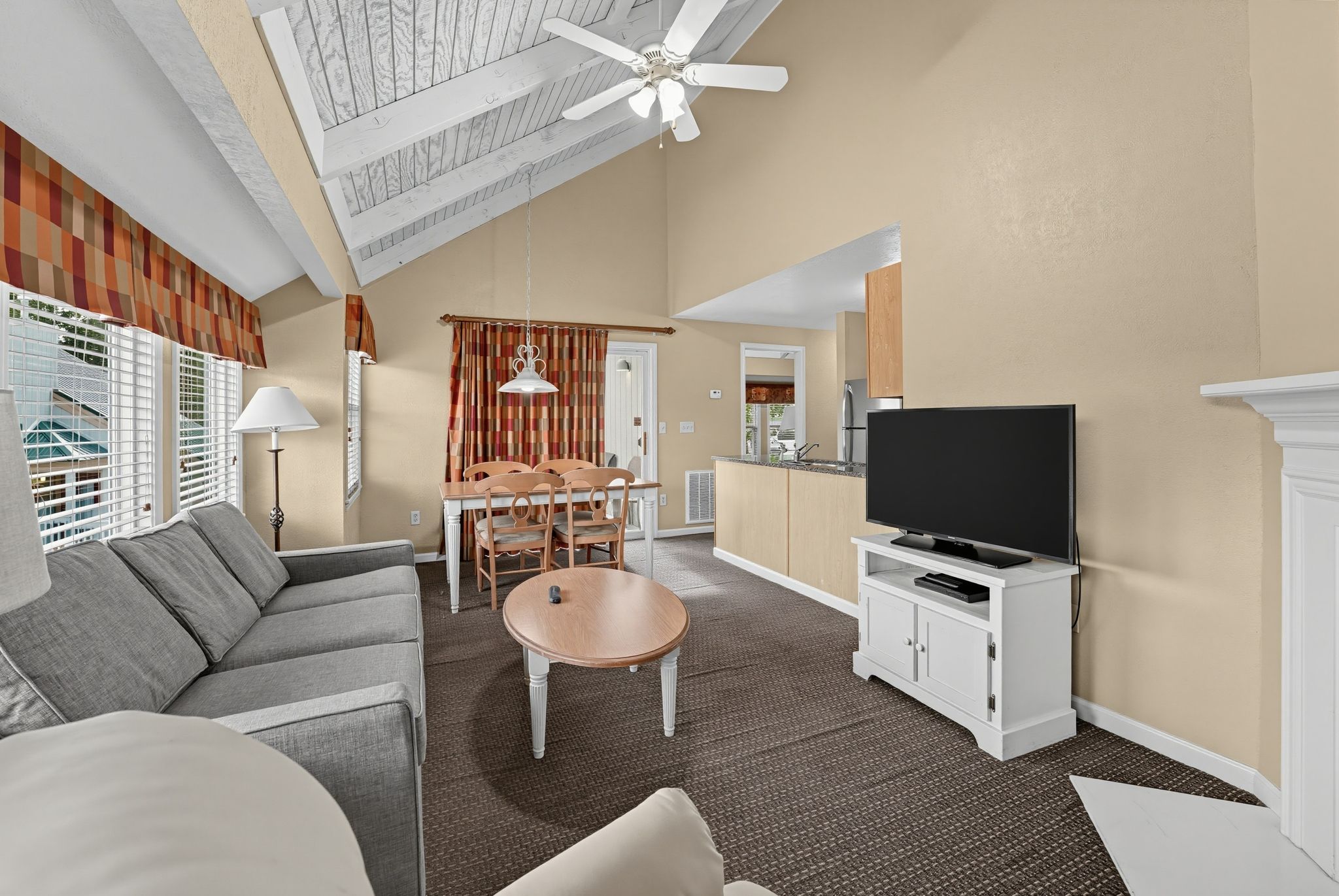 image Living room with a gray sofa, TV, and dining table under a vaulted ceiling with a ceiling fan.