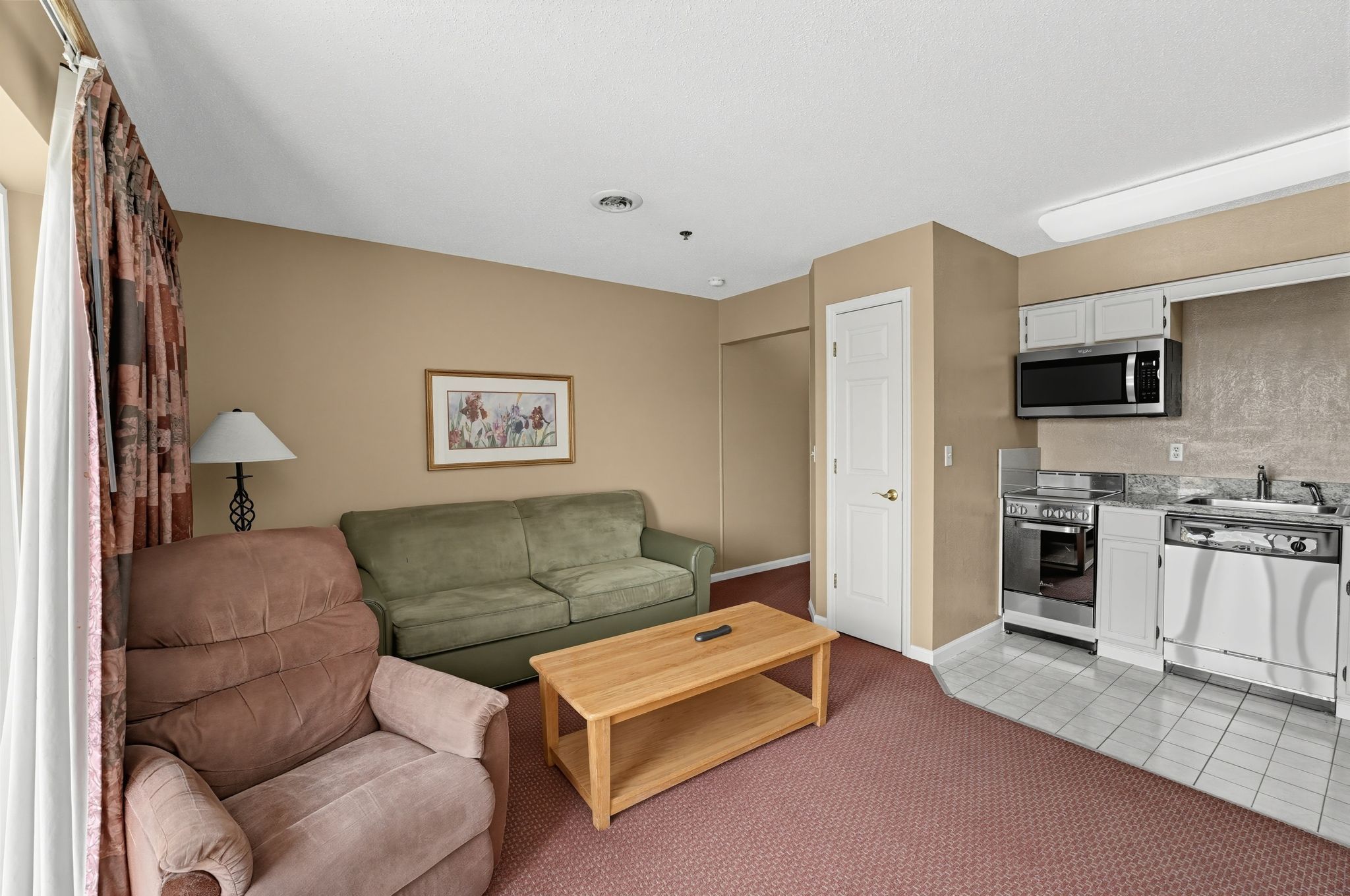 image Living area with a sofa, recliner, and coffee table, with a kitchen along the back wall.