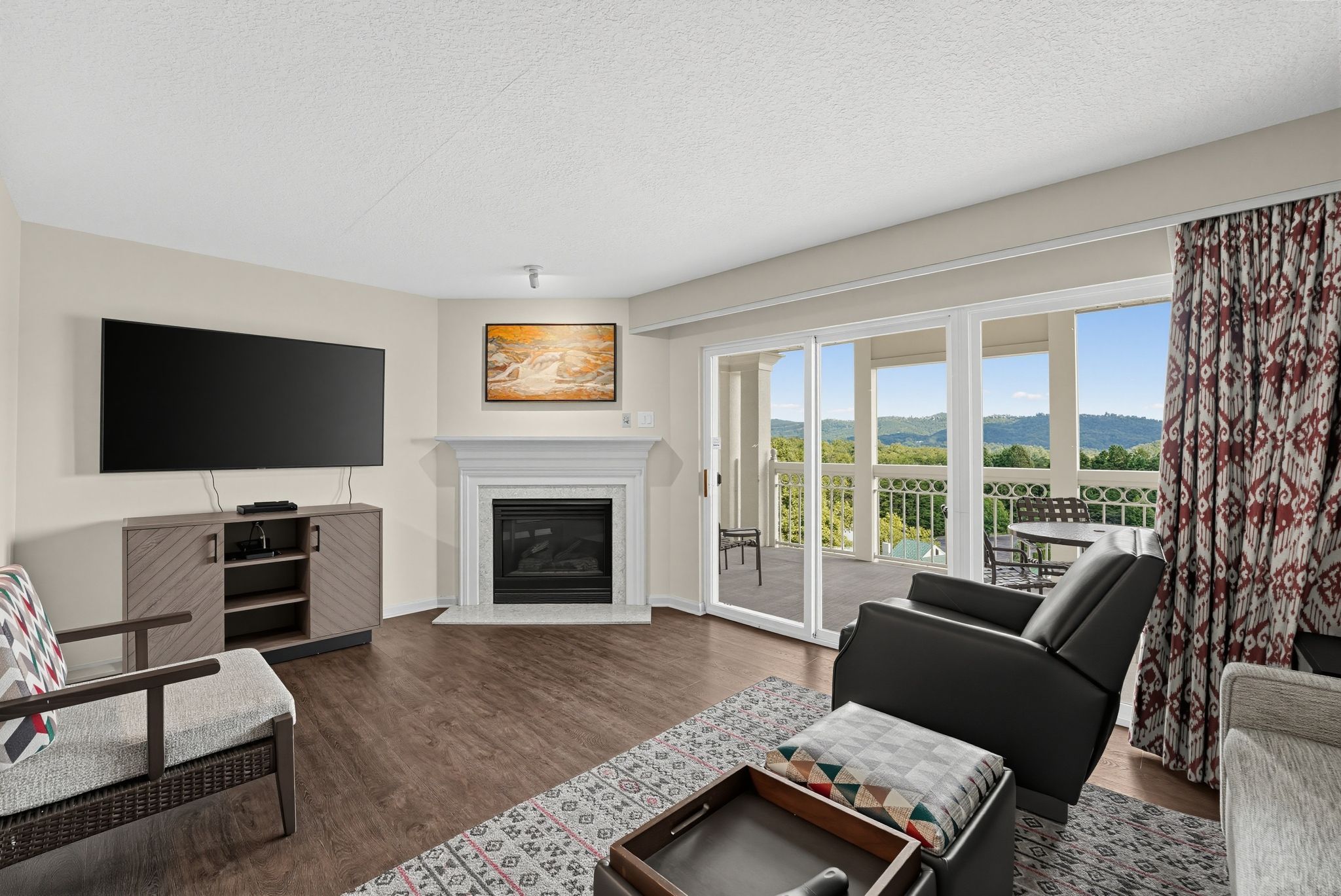 image Living room with a fireplace, wall-mounted TV, and armchairs, with sliding doors to a balcony.