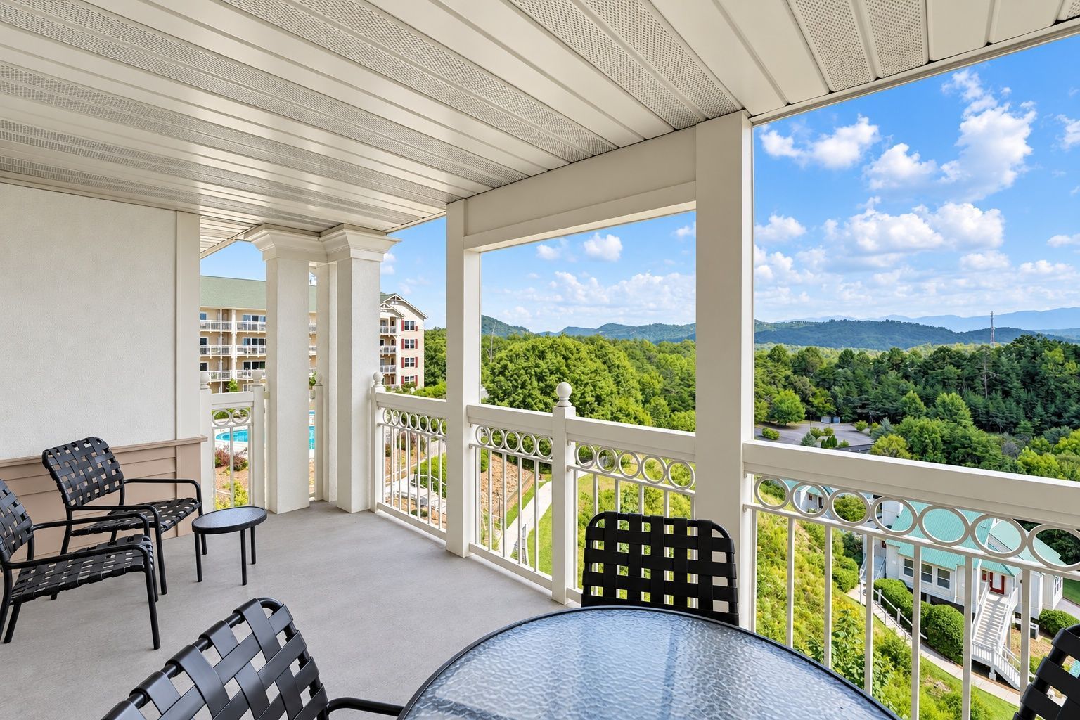image Covered balcony with patio chairs and a table overlooking green hills and distant mountains.