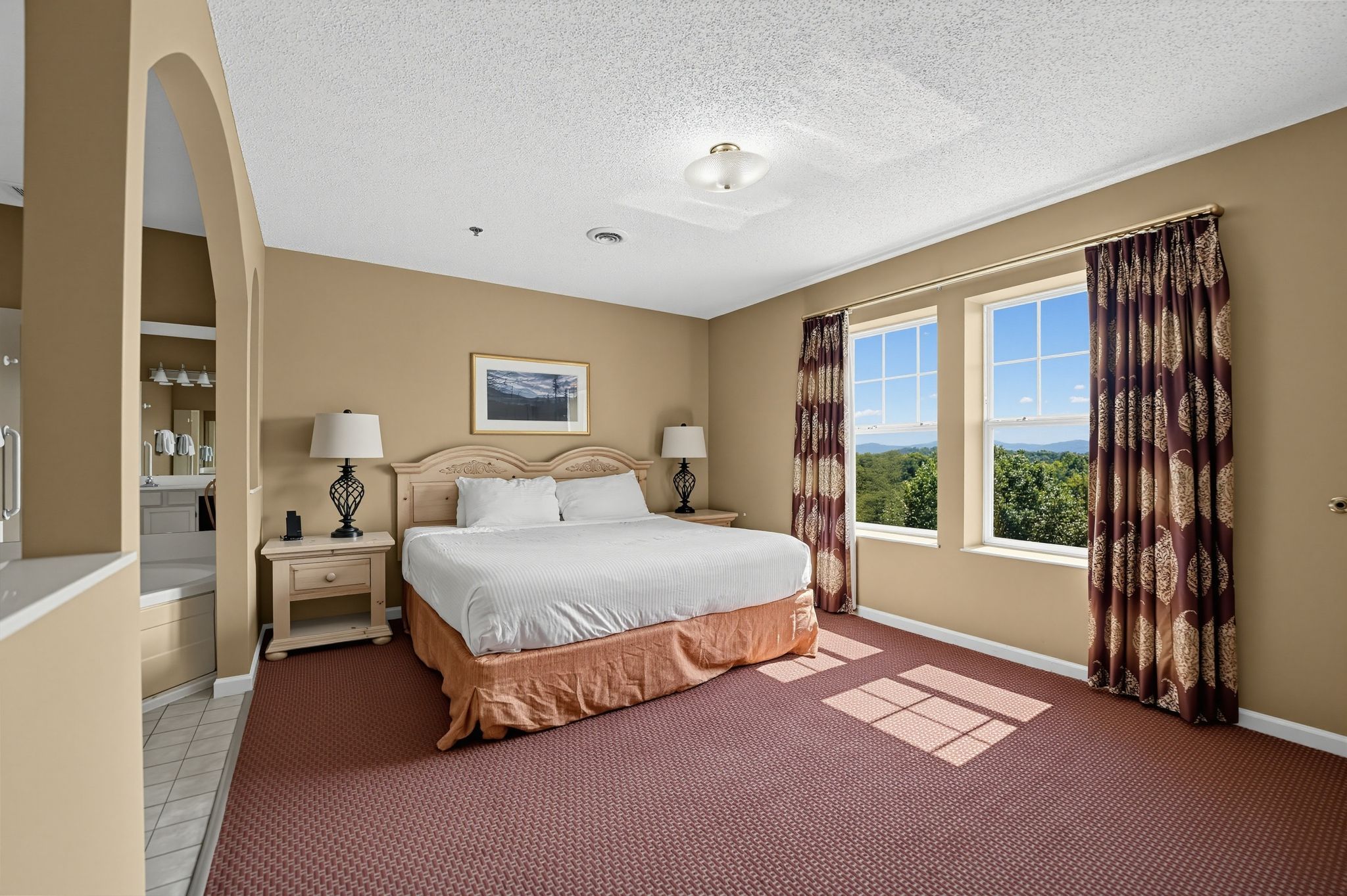 image Bedroom with a bed, nightstands with lamps, and windows overlooking trees and hills.