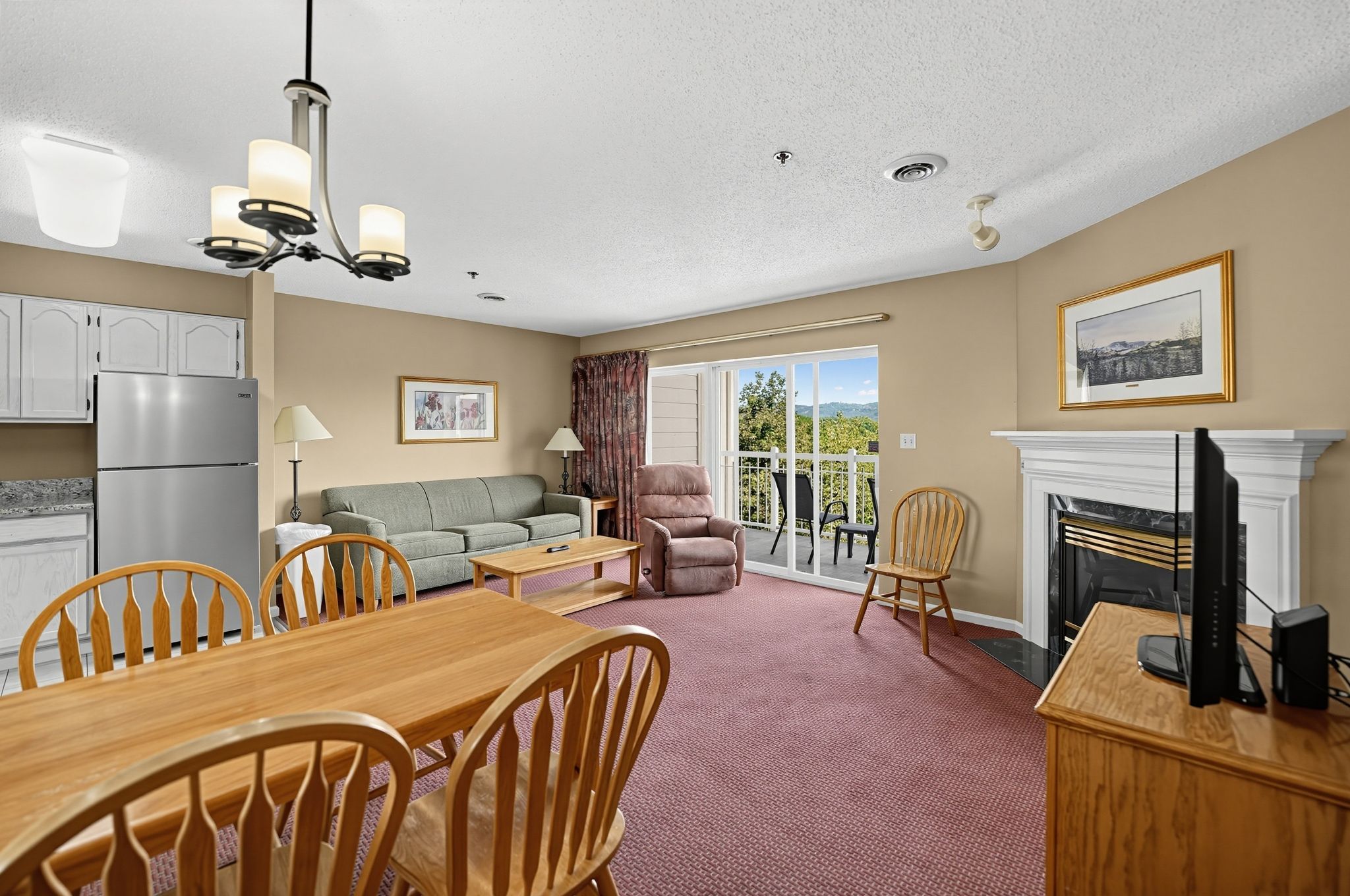 image Living area with a fireplace, TV, sofa, and a dining table beside the sliding balcony doors.