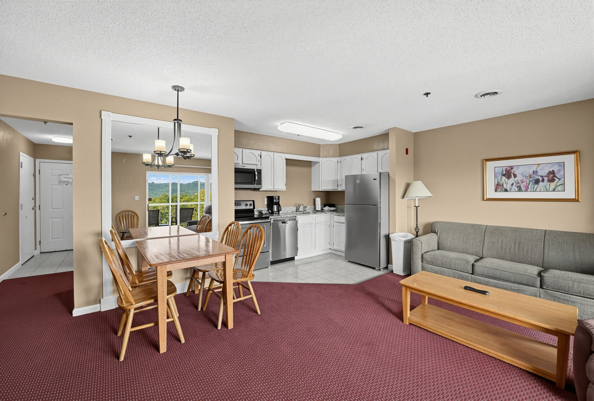 image Dining table, kitchen, and living area with a sofa, beside balcony doors.