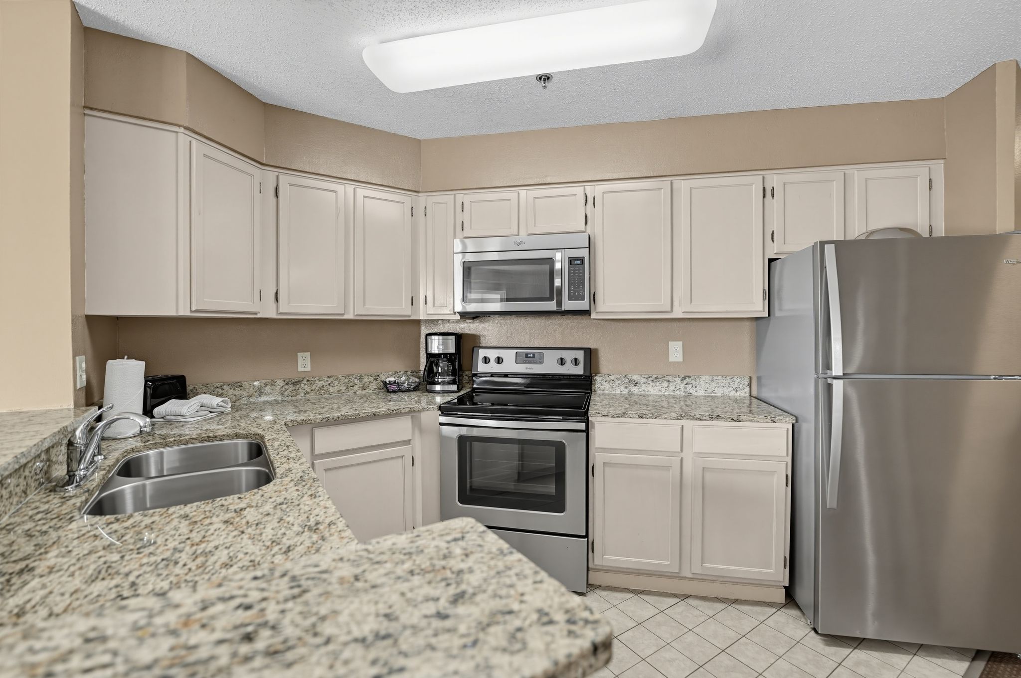 image Kitchen with a stainless steel refrigerator, range, and microwave, plus a double sink.