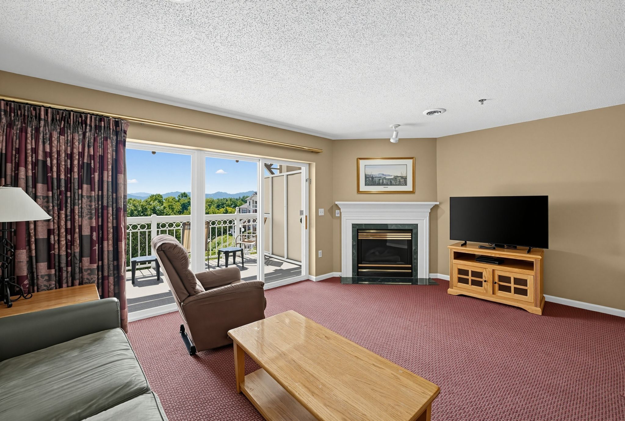 image Living room with a fireplace, TV, and recliner, with sliding doors to a balcony and mountain views.