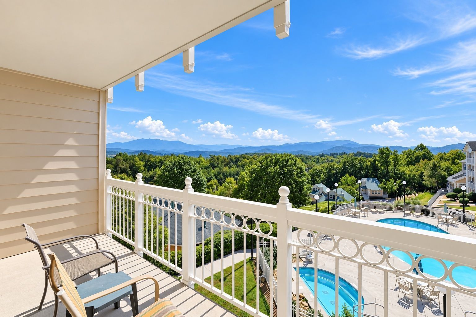 image Balcony with lounge chairs overlooking a pool area, green hills, and distant mountains.