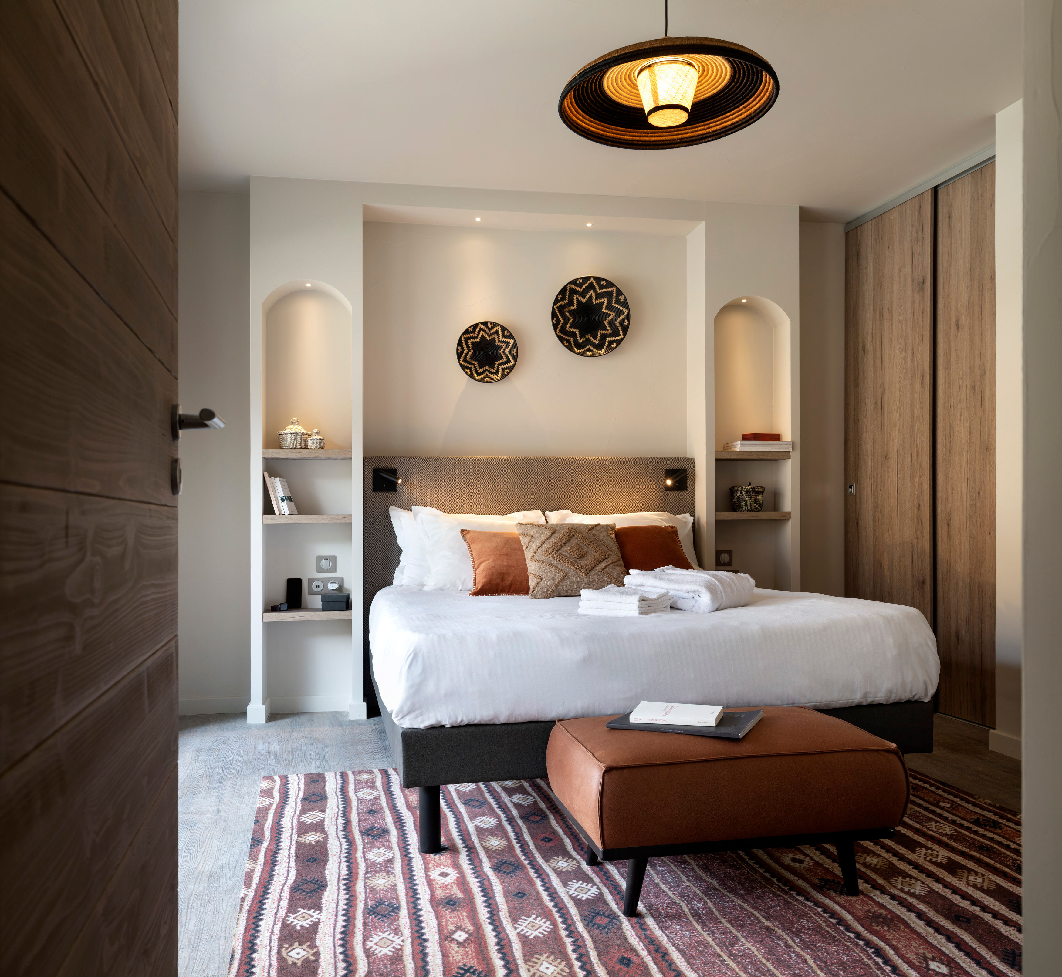 image White bedding and brown accent cushions dress the double bed, with wall niches and a patterned rug below.