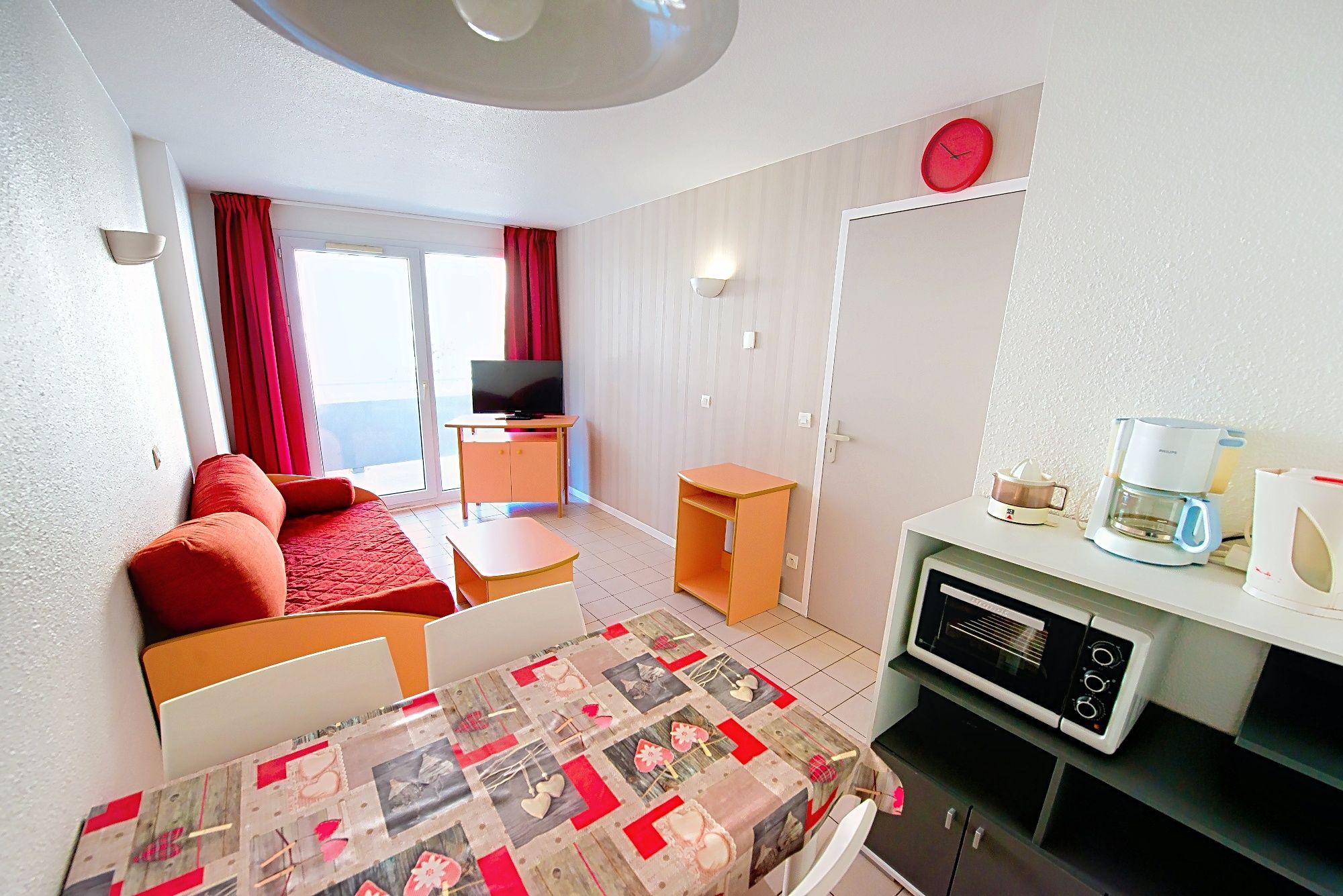 image Bright living area with a red sofa, TV and colourful curtains for easy evenings.