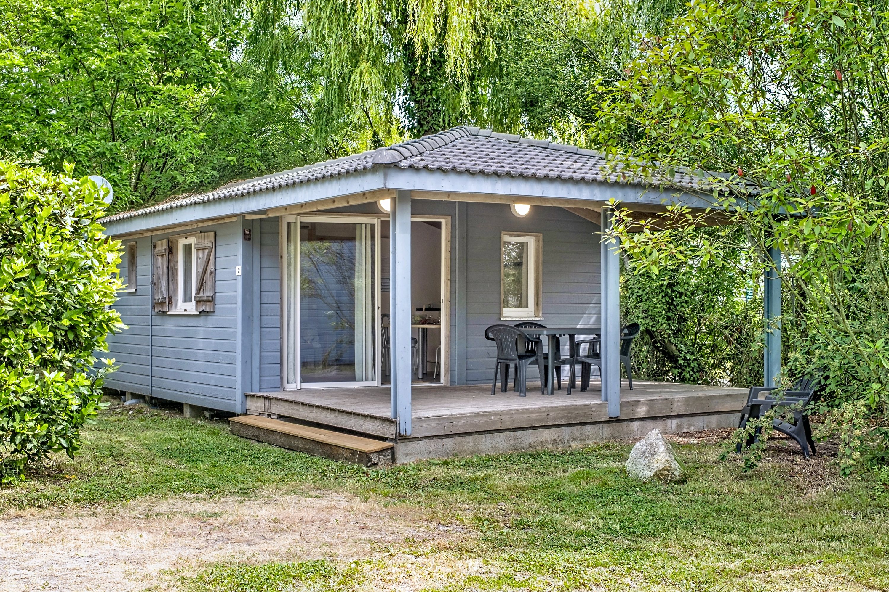 image Light blue siding and a sloped roof give the cottage its seaside look, with chairs waiting on the porch.