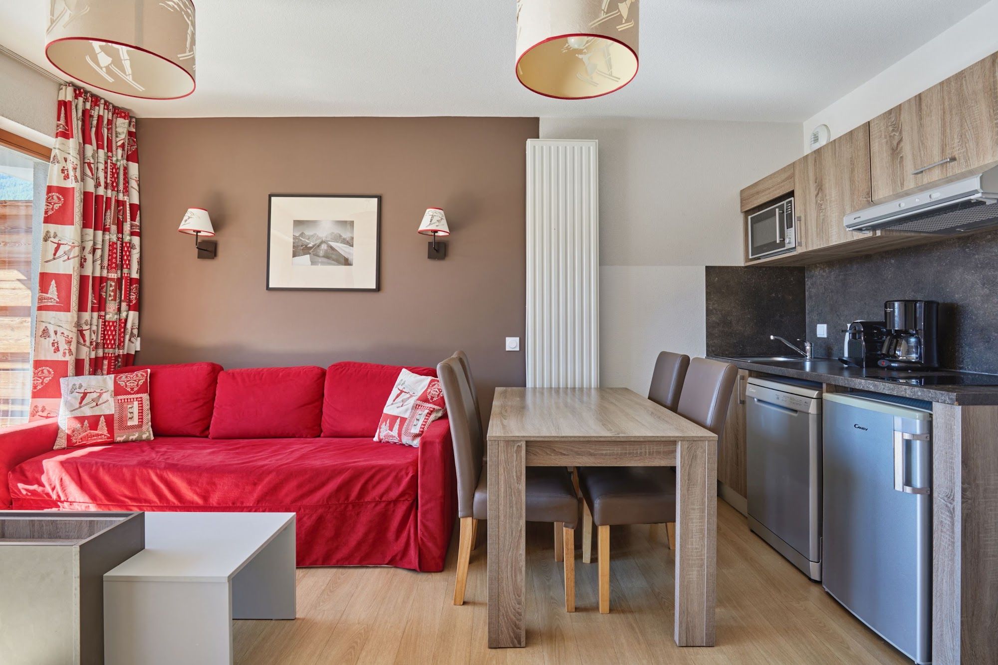 image Living area with a red sofa, dining table and kitchenette behind