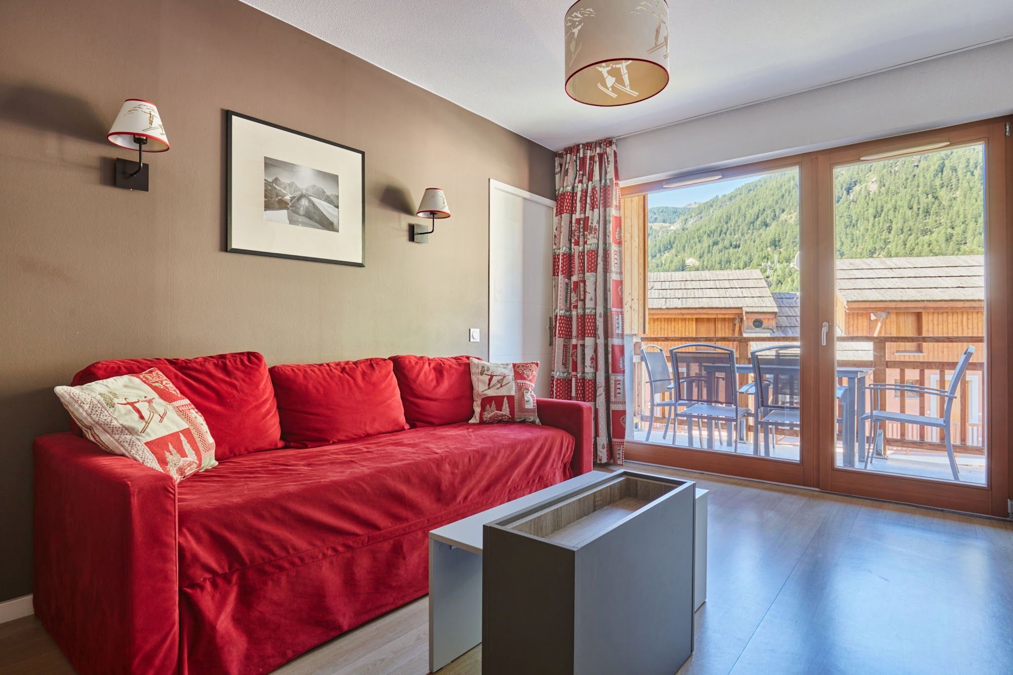 image Red sofa with ski-themed cushions beside patterned curtains