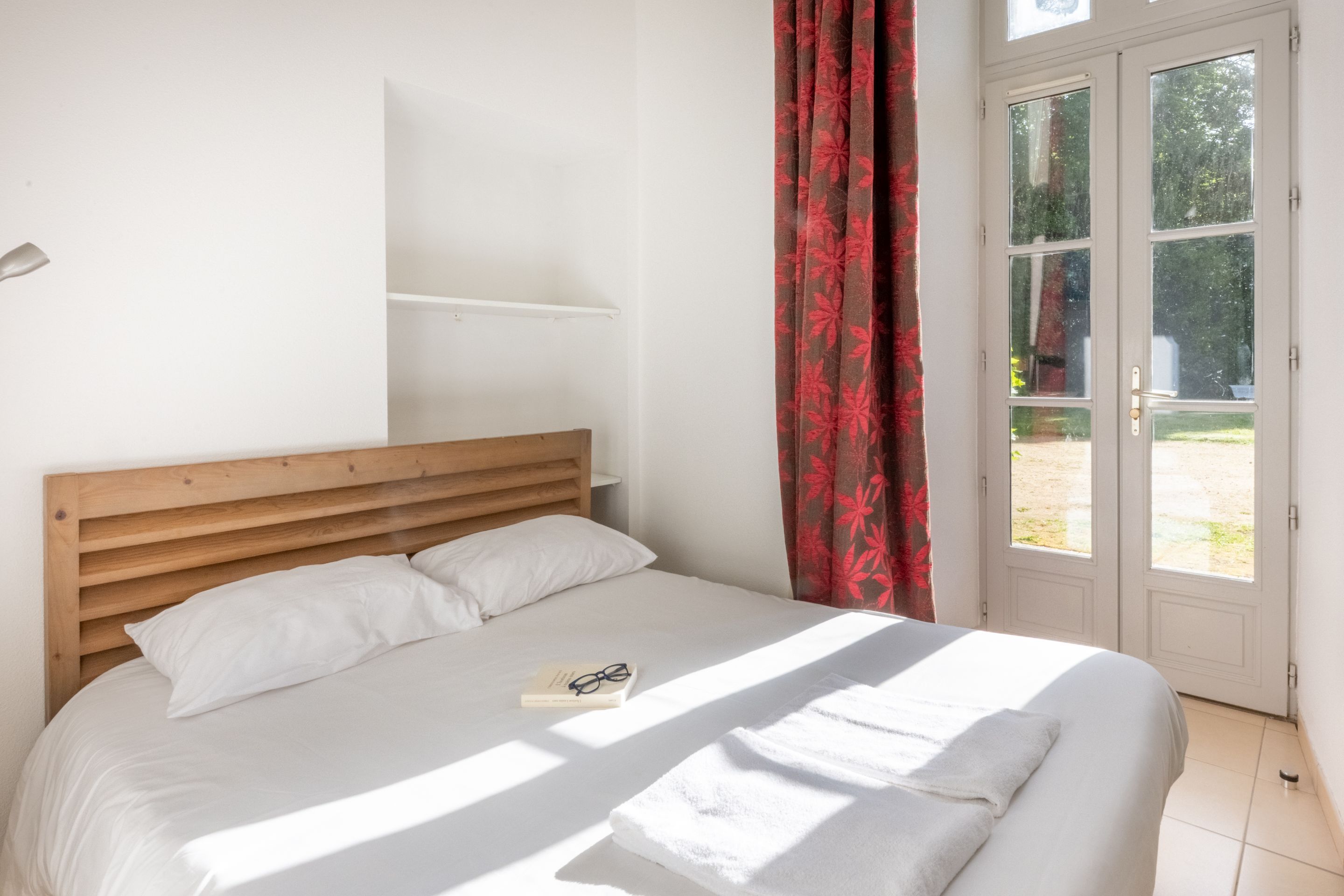 image Red floral curtains bring color to the bedroom, framing a wooden headboard and crisp white linens.
