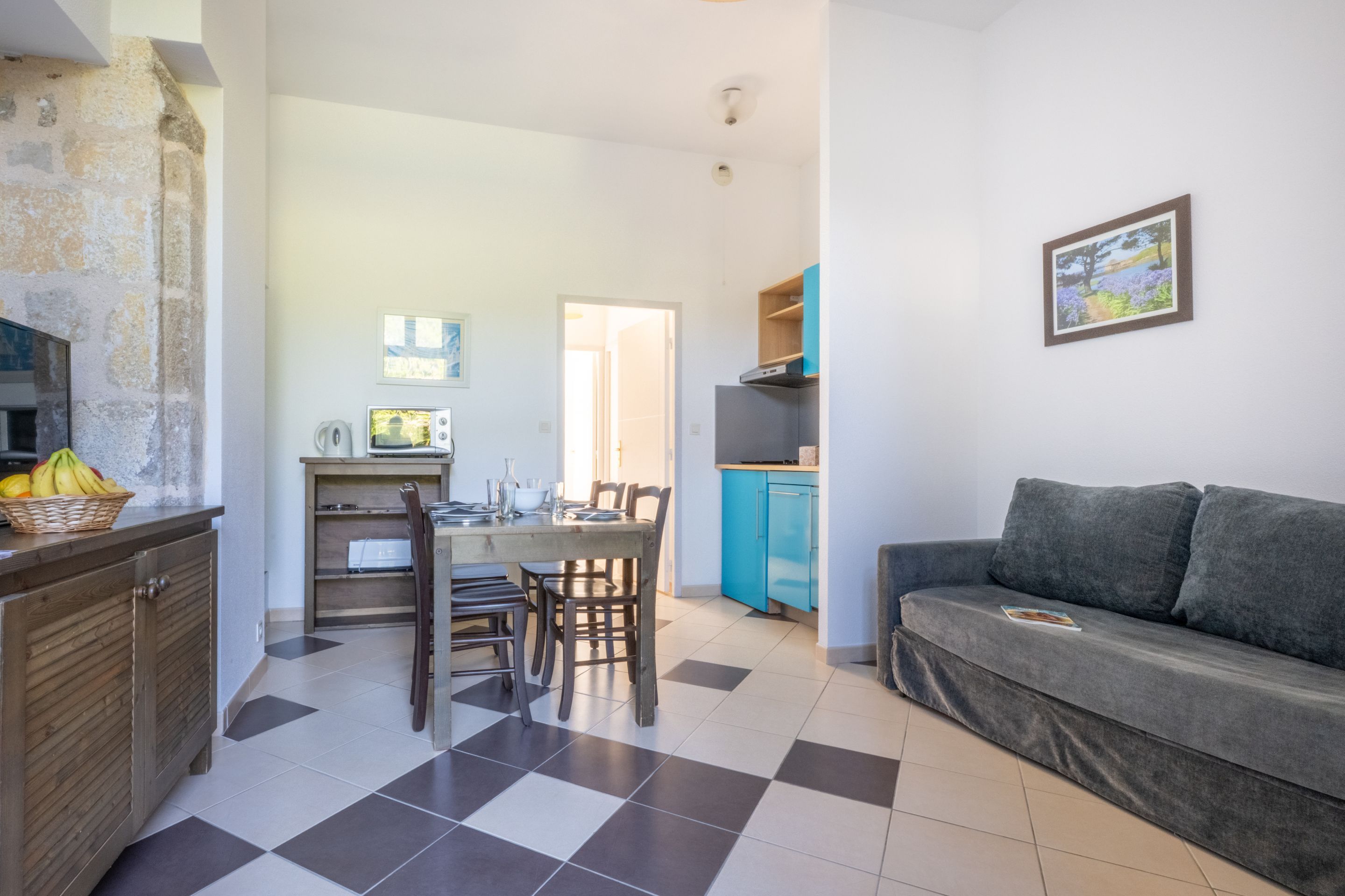 image A stone accent wall anchors the open living space, alongside a grey sofa and blue kitchen cabinets.