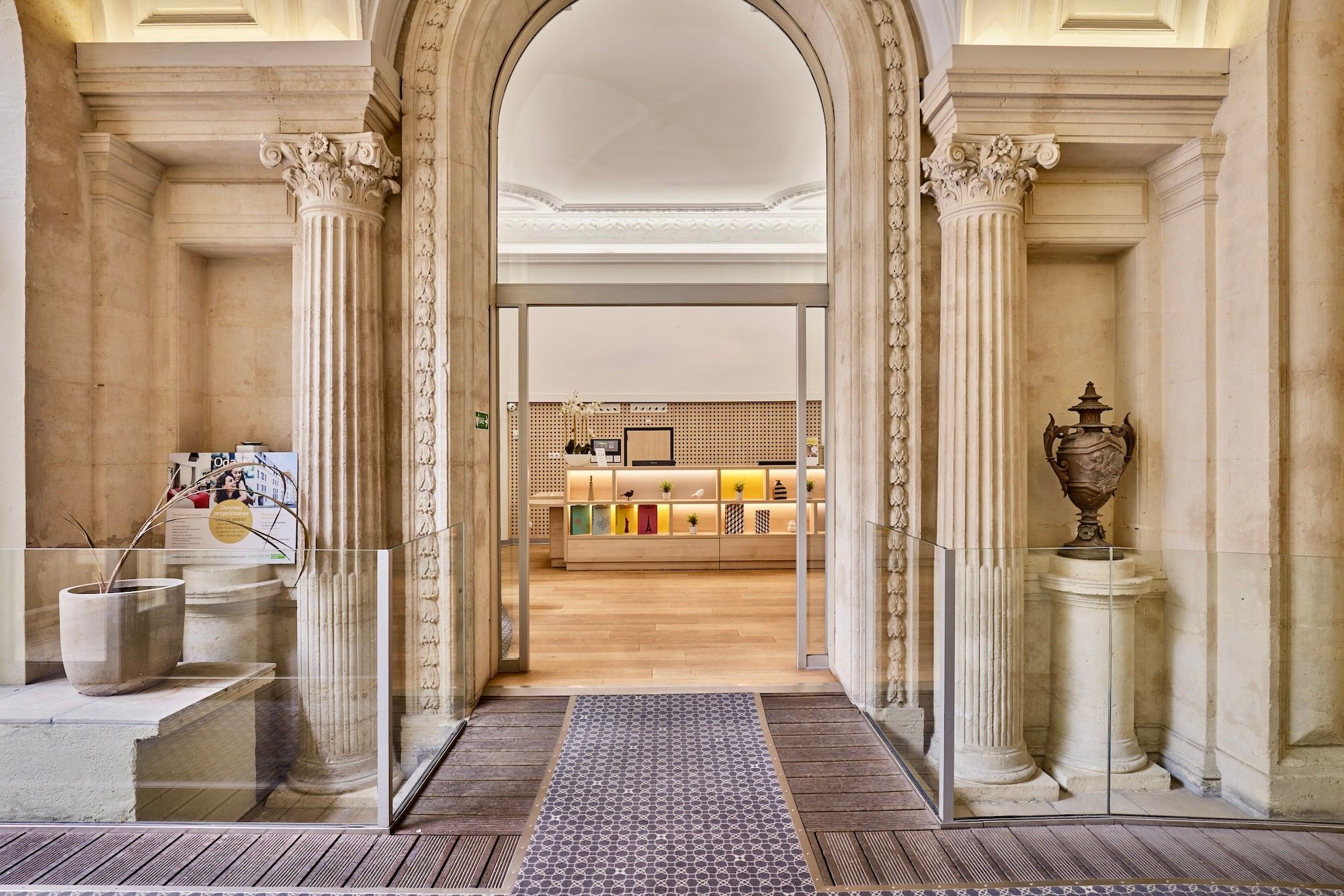 image Pass through a stately corridor framed by stone columns and sculptures into a warm, modern reception area.