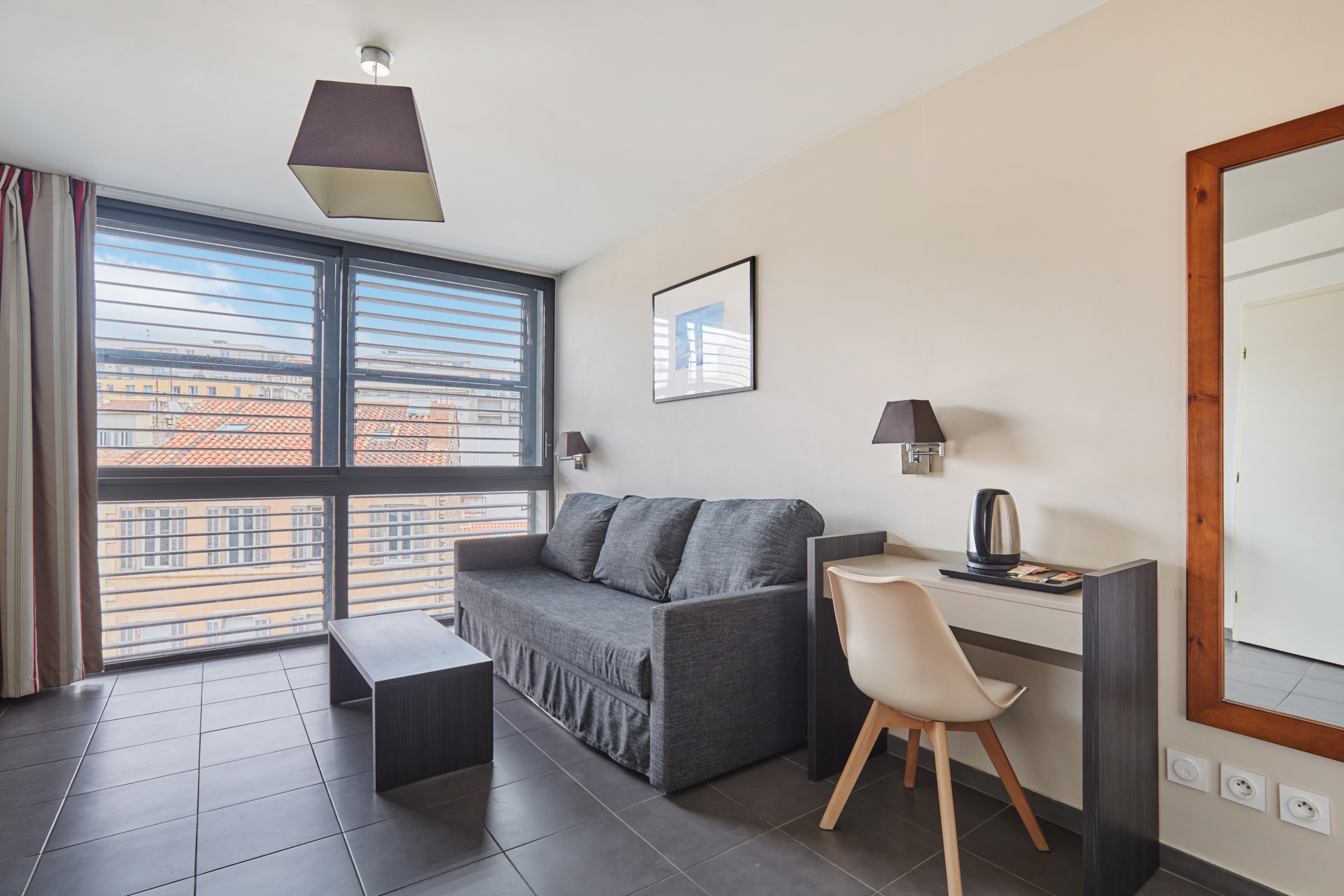 image Step into this inviting living space, where modern design meets comfort with a cozy sofa and sleek desk, all bathed in natural light from expansive windows.