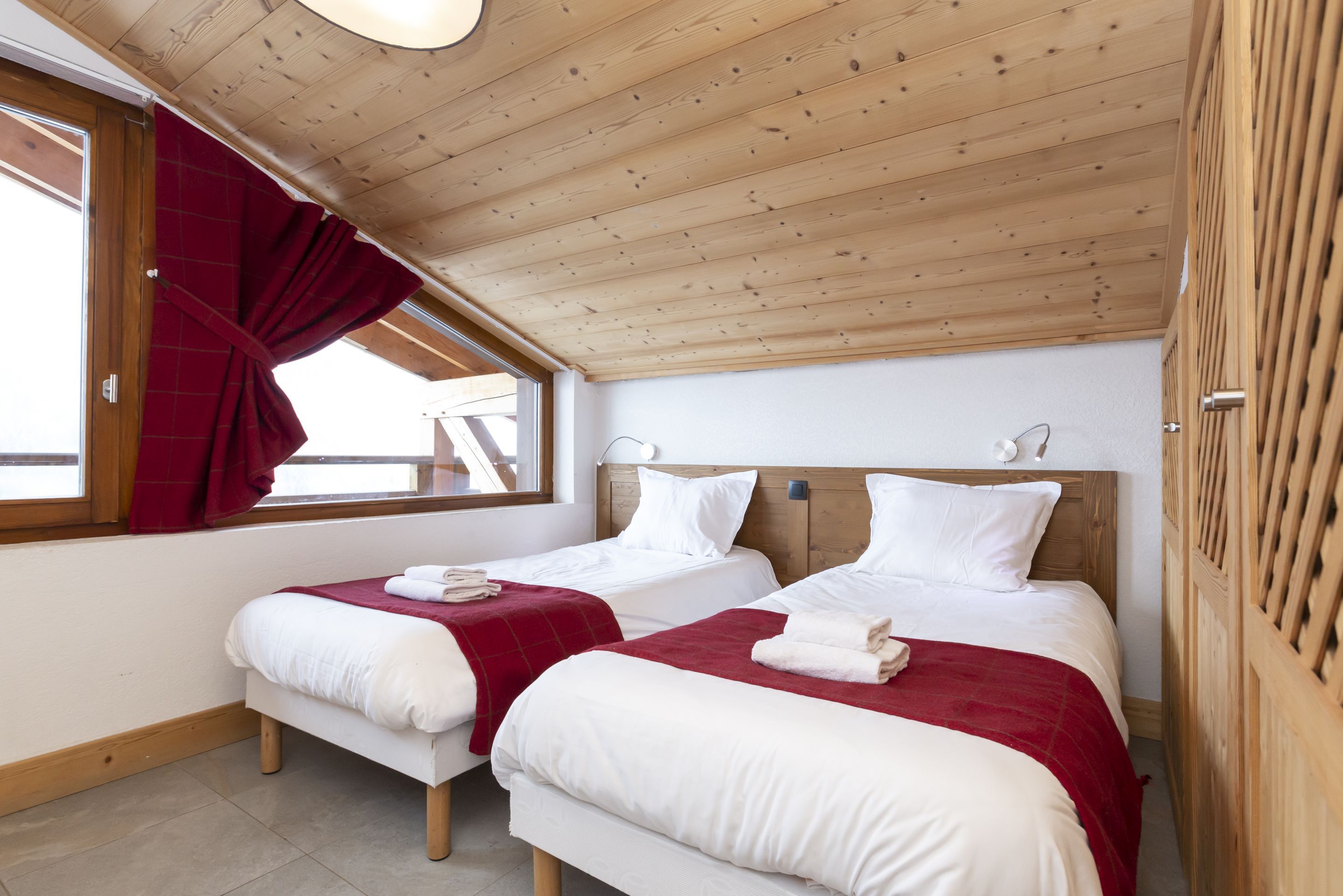 image The twin bedroom with red throws and a wooden wardrobe — warm and practical for a ski week at altitude.