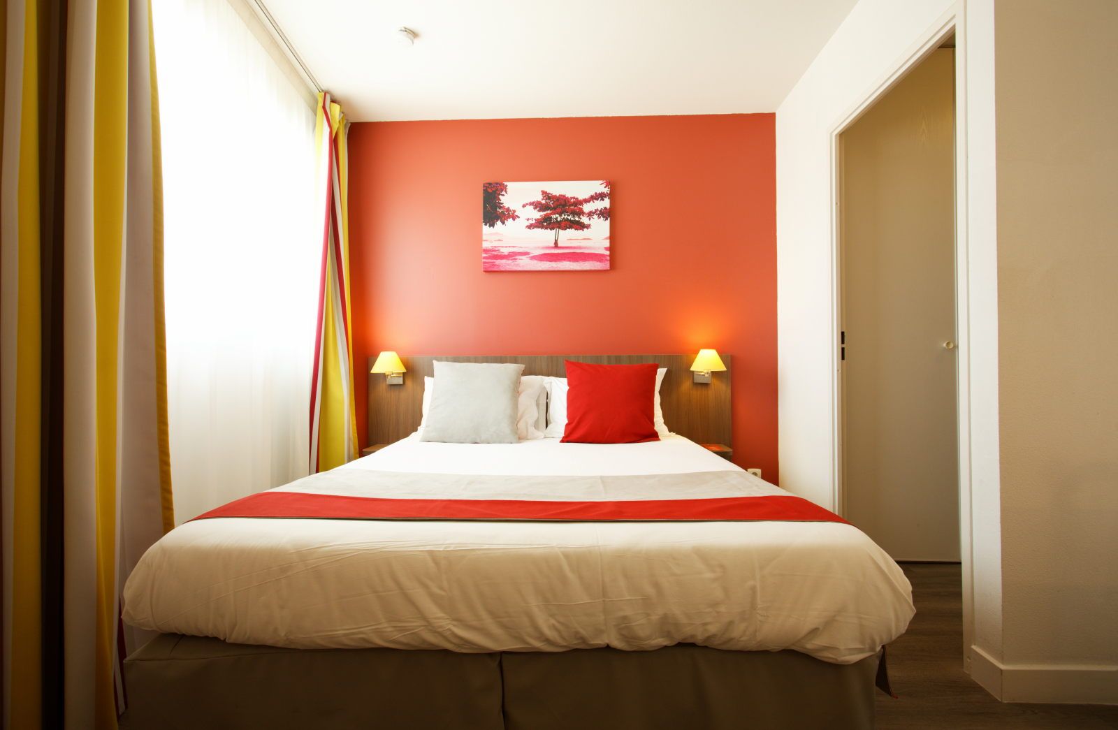 image Bed with red and gray pillows against a colorful wall with ample natural light