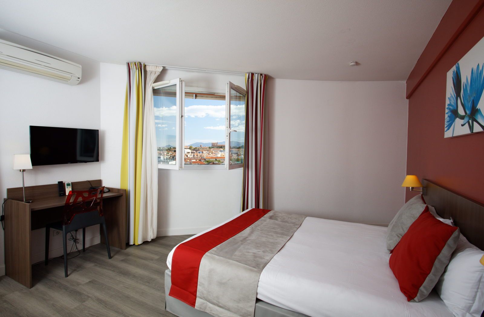 image Studio bed with red and gray decorative blanket and a window offering a city view