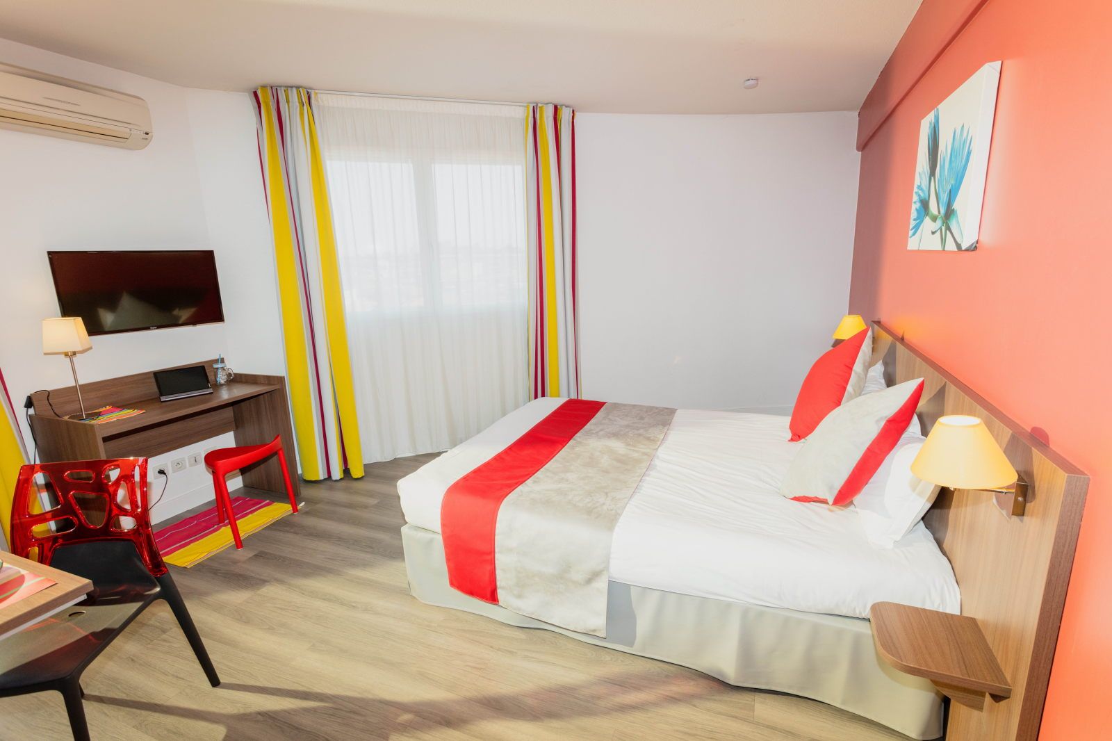 image Studio bed with red and gray bedding alongside a flat-screen TV