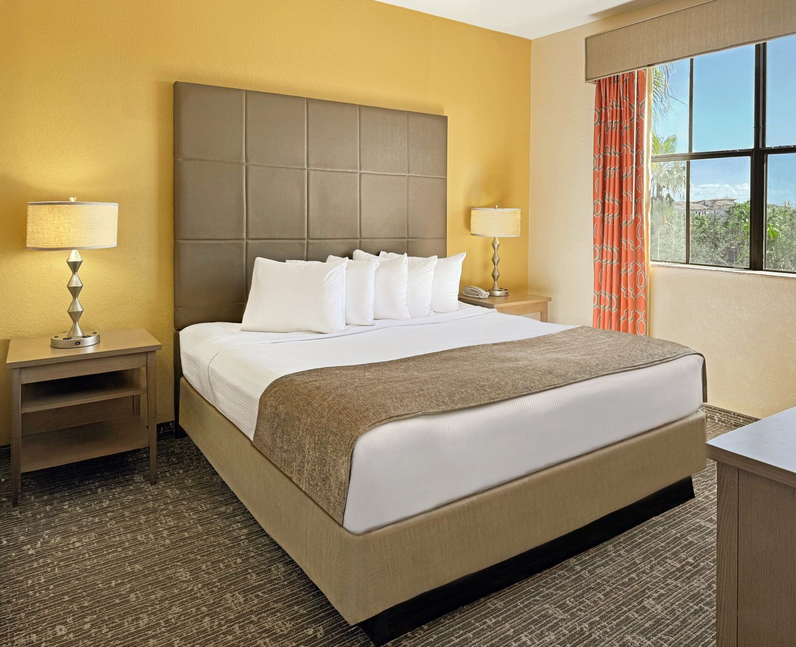 image King bed with a decorative headboard, bedside tables, and a large curtained window letting in natural light