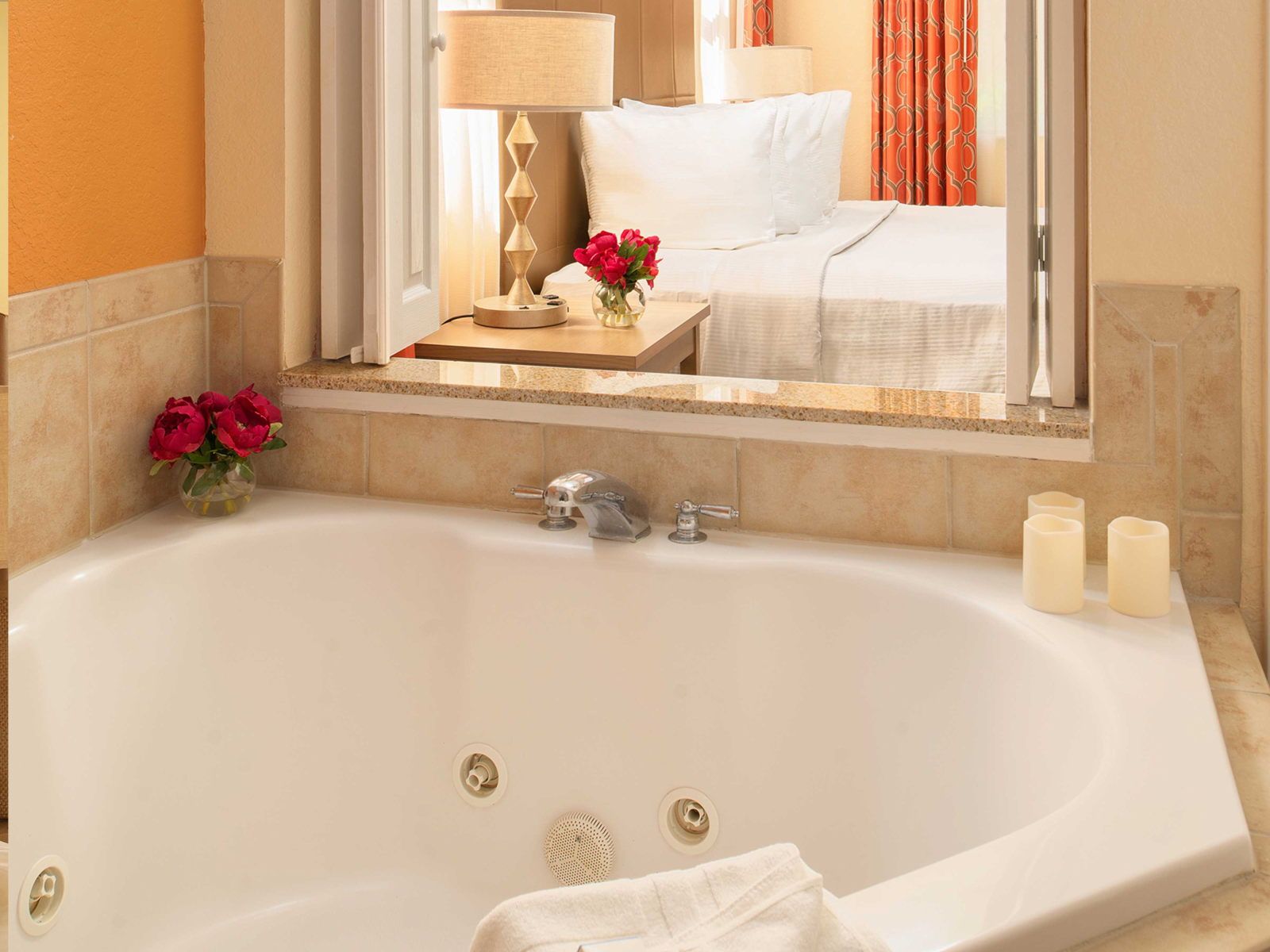 image Soak in the corner Jacuzzi tub — chrome taps, travertine surround, and a pass-through window into the king bedroom behind