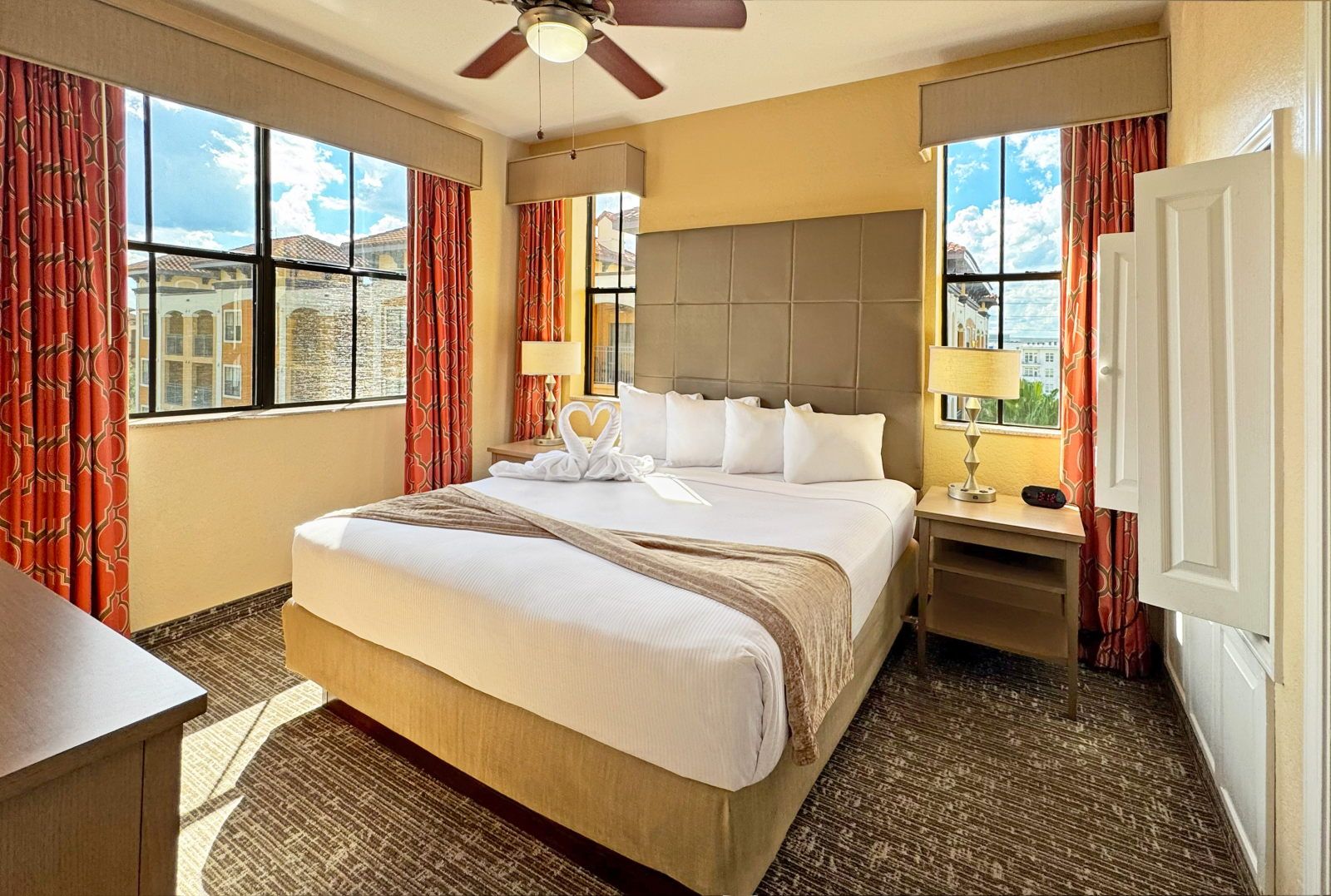 image King bed with white linens, decorative headboard, warm-toned curtains, and bedside lamps on both sides