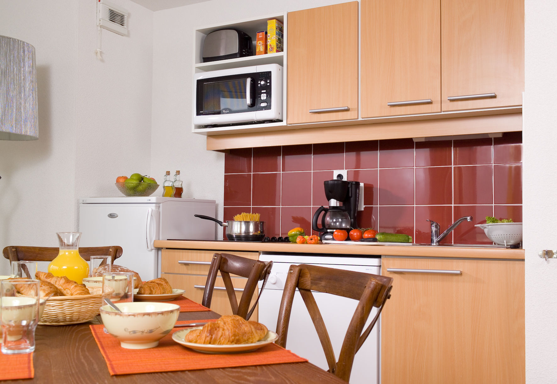 image Dining table for four beside a kitchenette with refrigerator, stovetop, microwave, toaster, and coffee maker