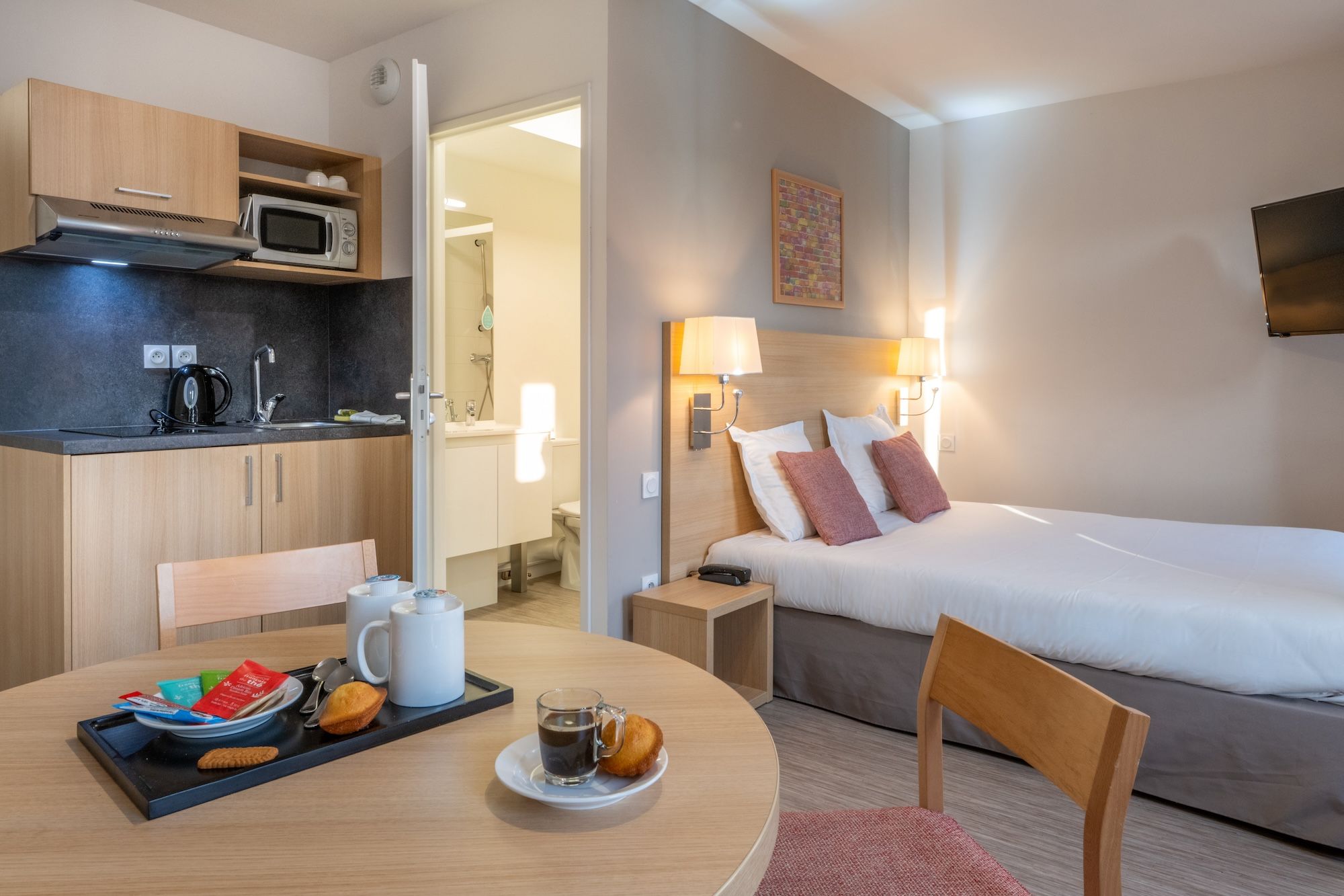 image A neatly arranged room featuring a small dining area, cozy bedding, and a glimpse of an adjacent bathroom.
