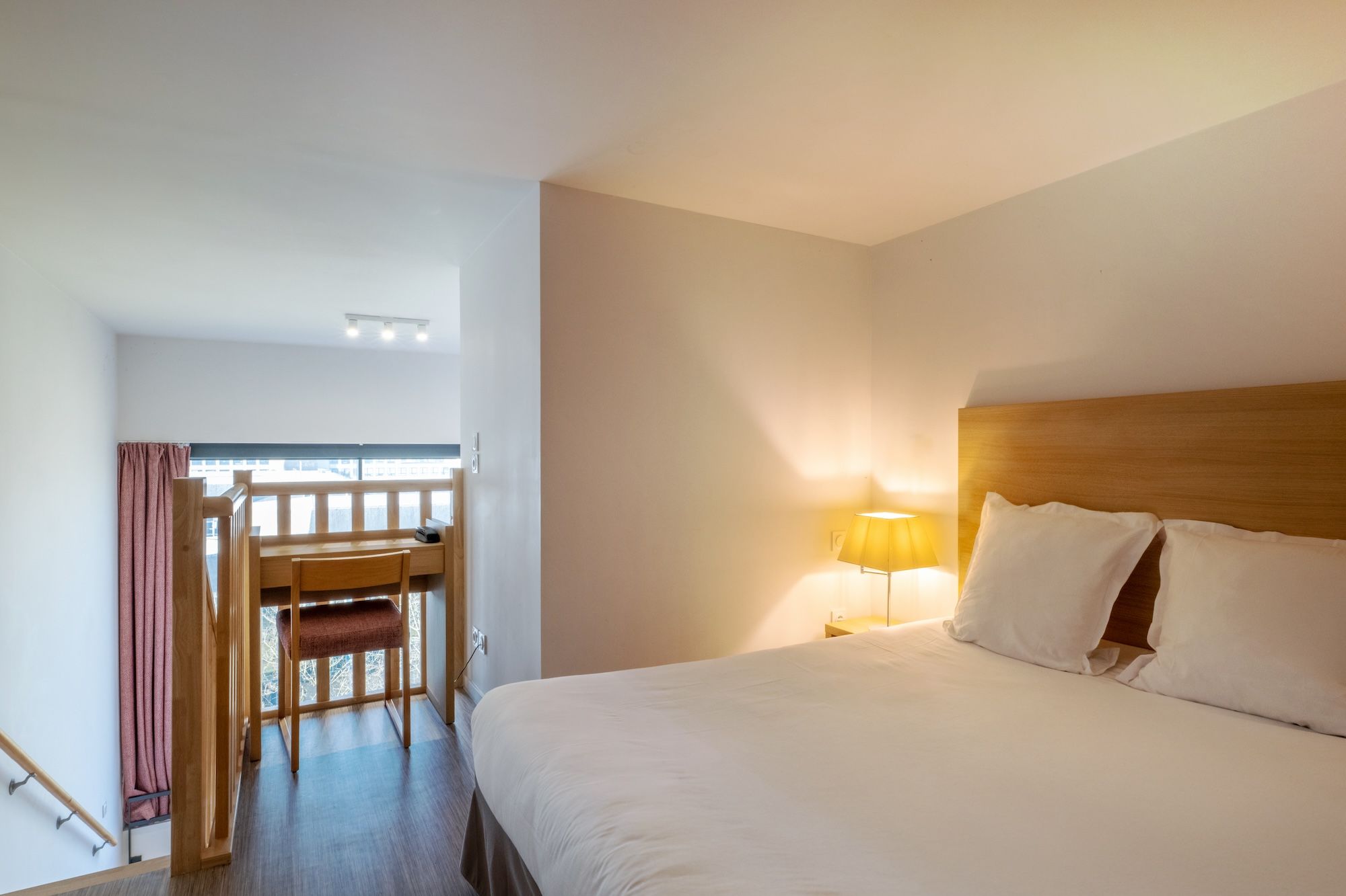 image A serene bedroom featuring a comfortable bed and a small writing desk, illuminated by a warm lamp.