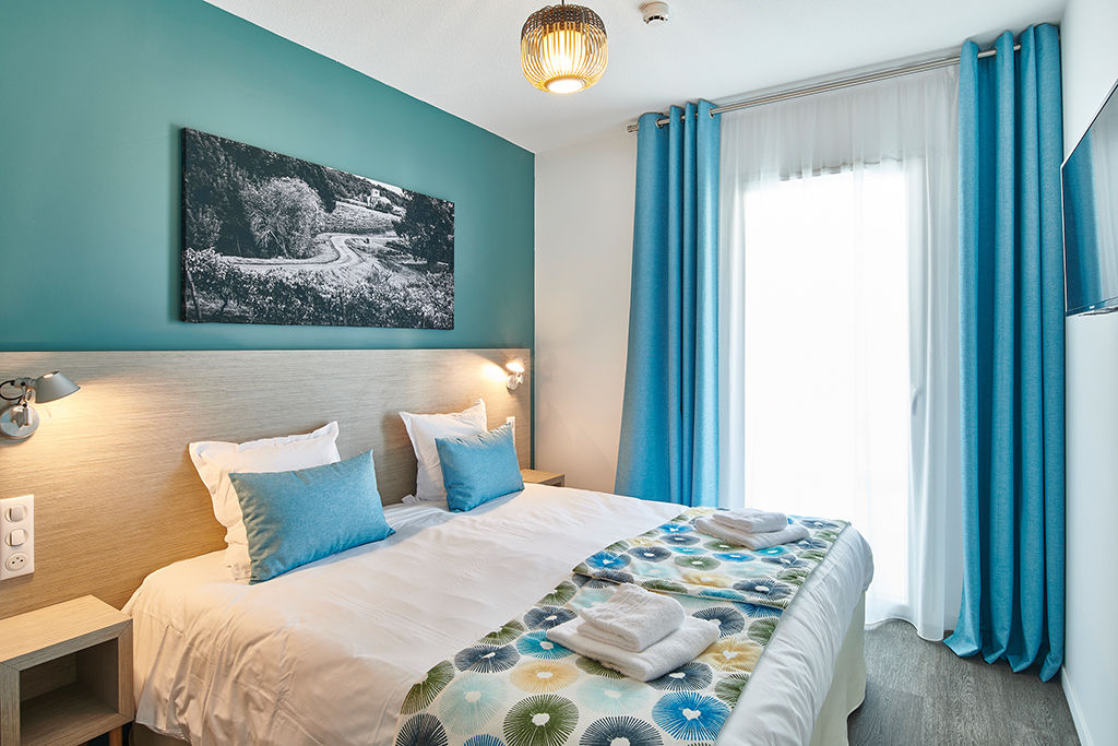 image Wake up in the double bed, framed by blue curtains and a piece of artwork on the wall