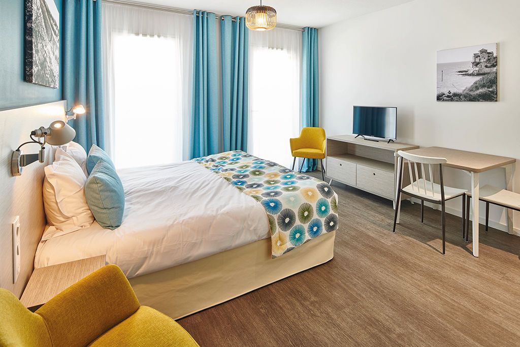 image A bed, a TV, a desk and a yellow chair fill this bedroom