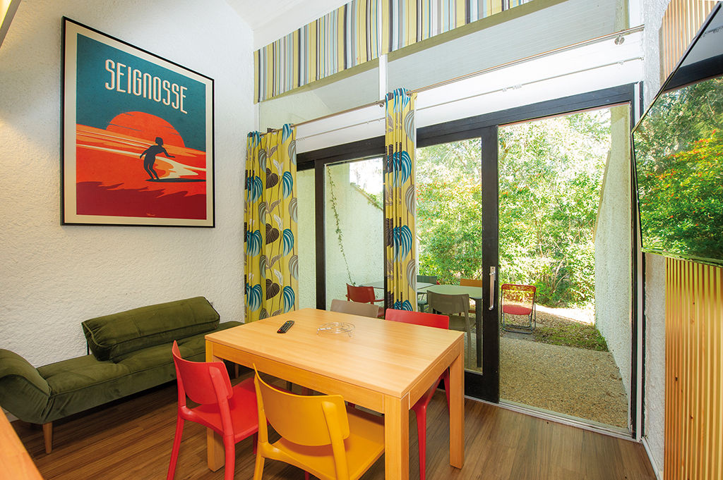 image Yellow, red and natural wood chairs surround the dining table, with a green sofa, a large framed poster and a glass door to the patio