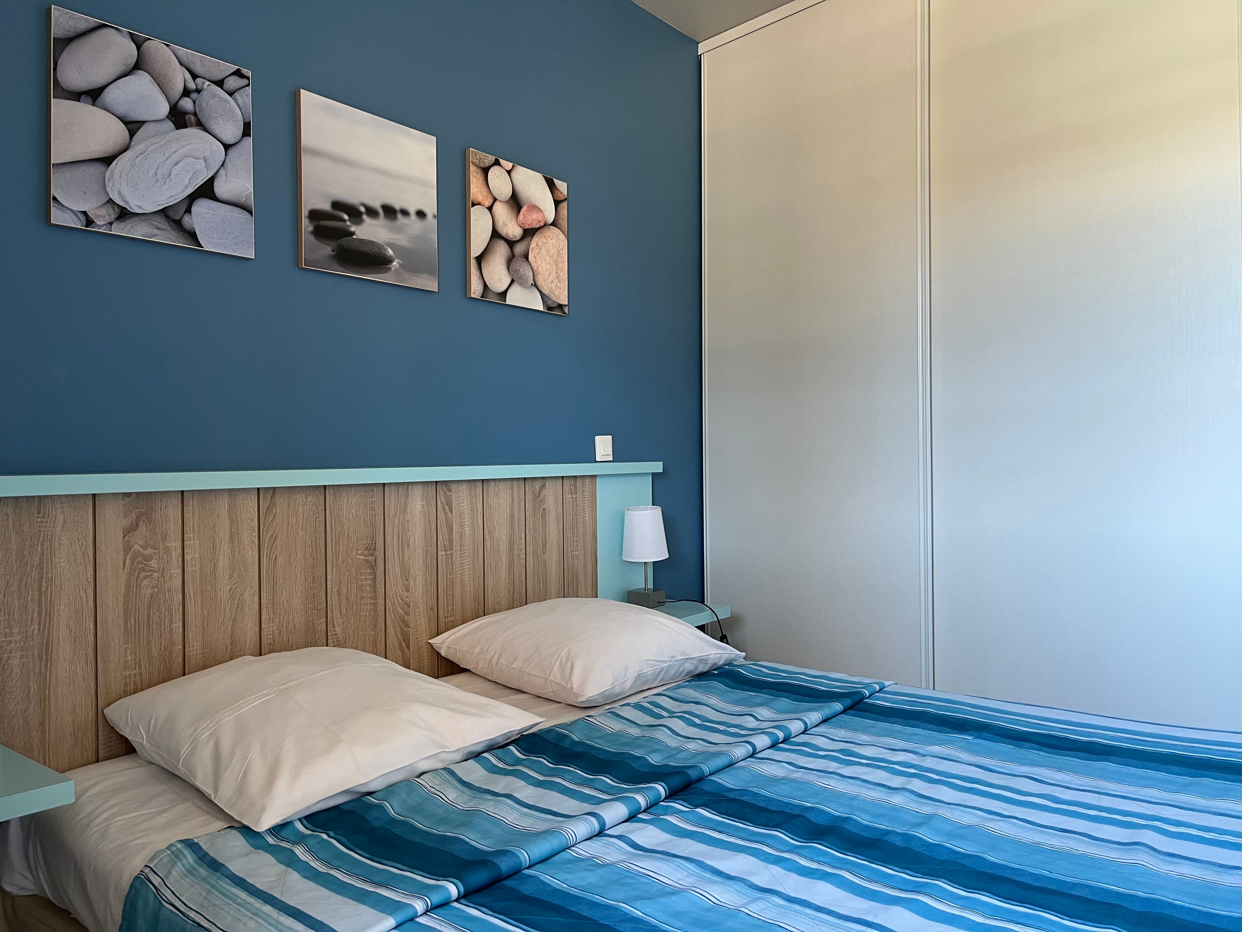 image Blue-toned double bedroom with wood-panel headboard — quiet and air-conditioned after sun-soaked days.