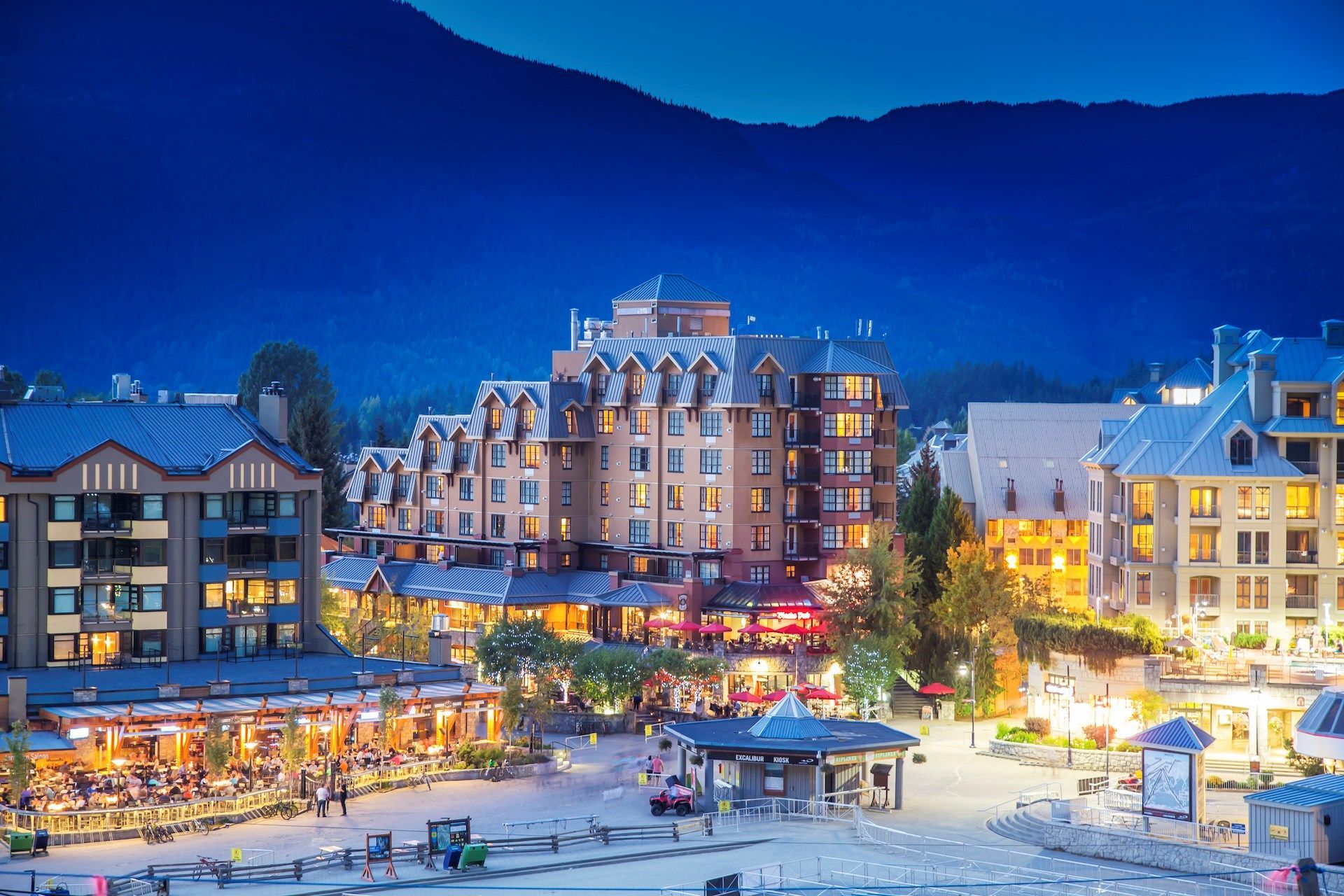 image Charming village square illuminated by soft evening lights, framed by majestic mountain silhouettes.